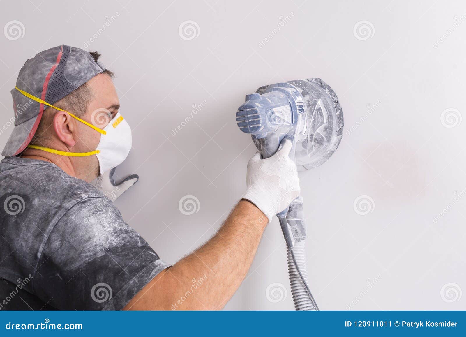 plasterer wearing dust mask polishes a wall with sanding machine