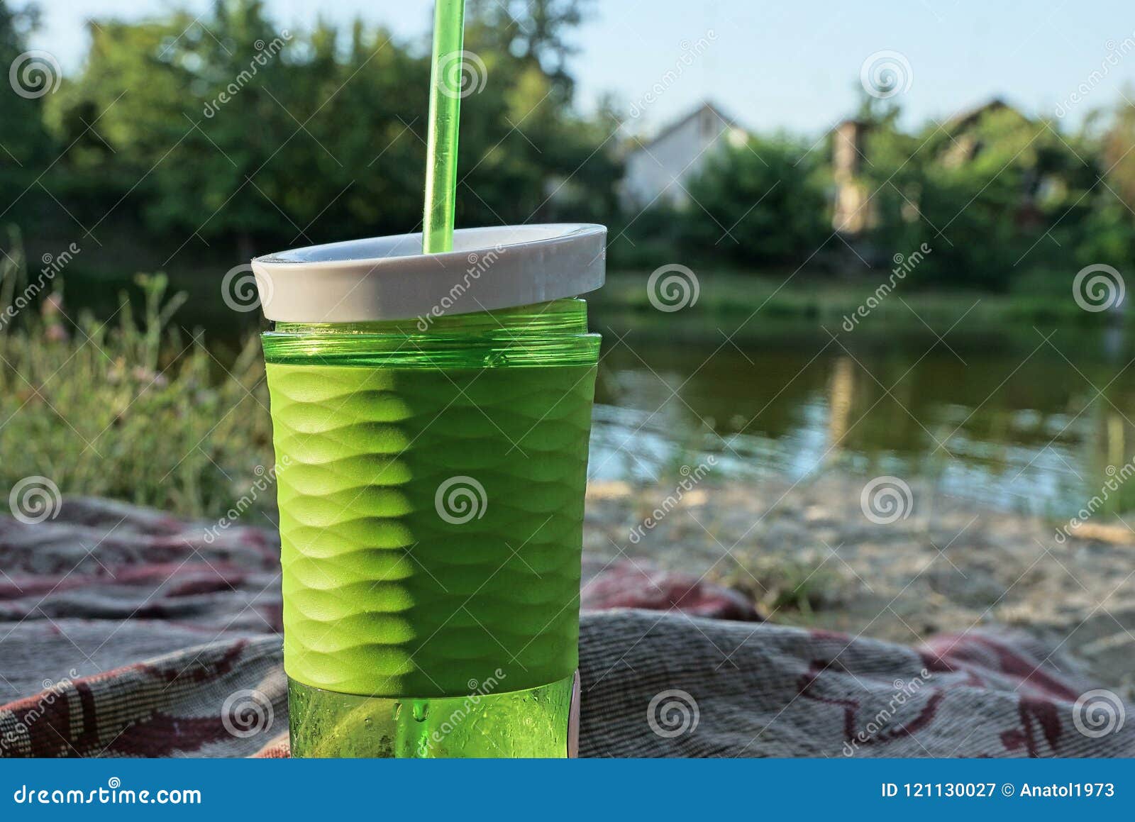 Plastic green glass with a drink and a tube on the beach near the water. A large plastic green glass with a drink and a tube on the shore near the water