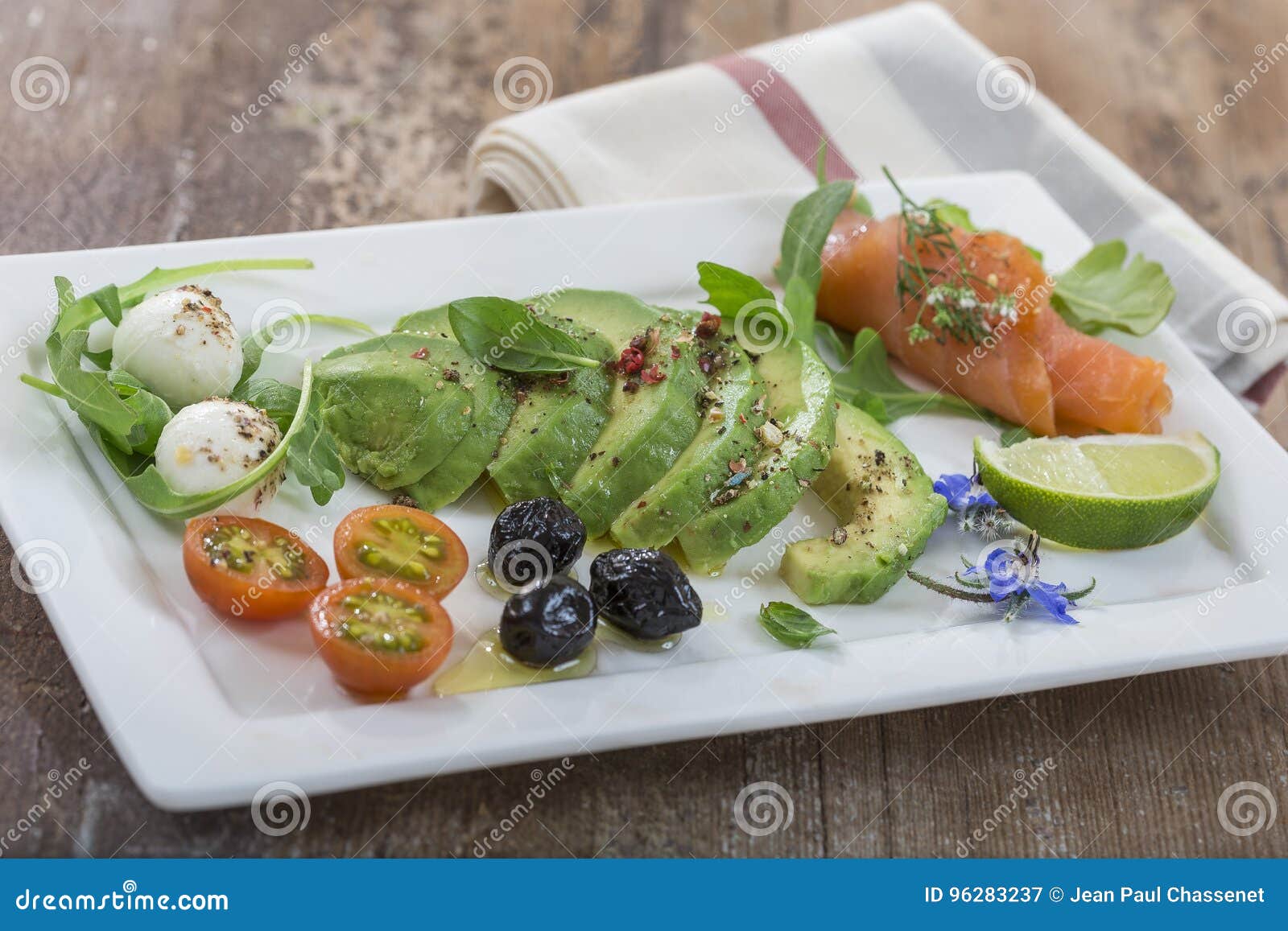 plate of sliced avocado and salmon toast bread with spices and mozzarella on dishcloth with borage, tomato and black