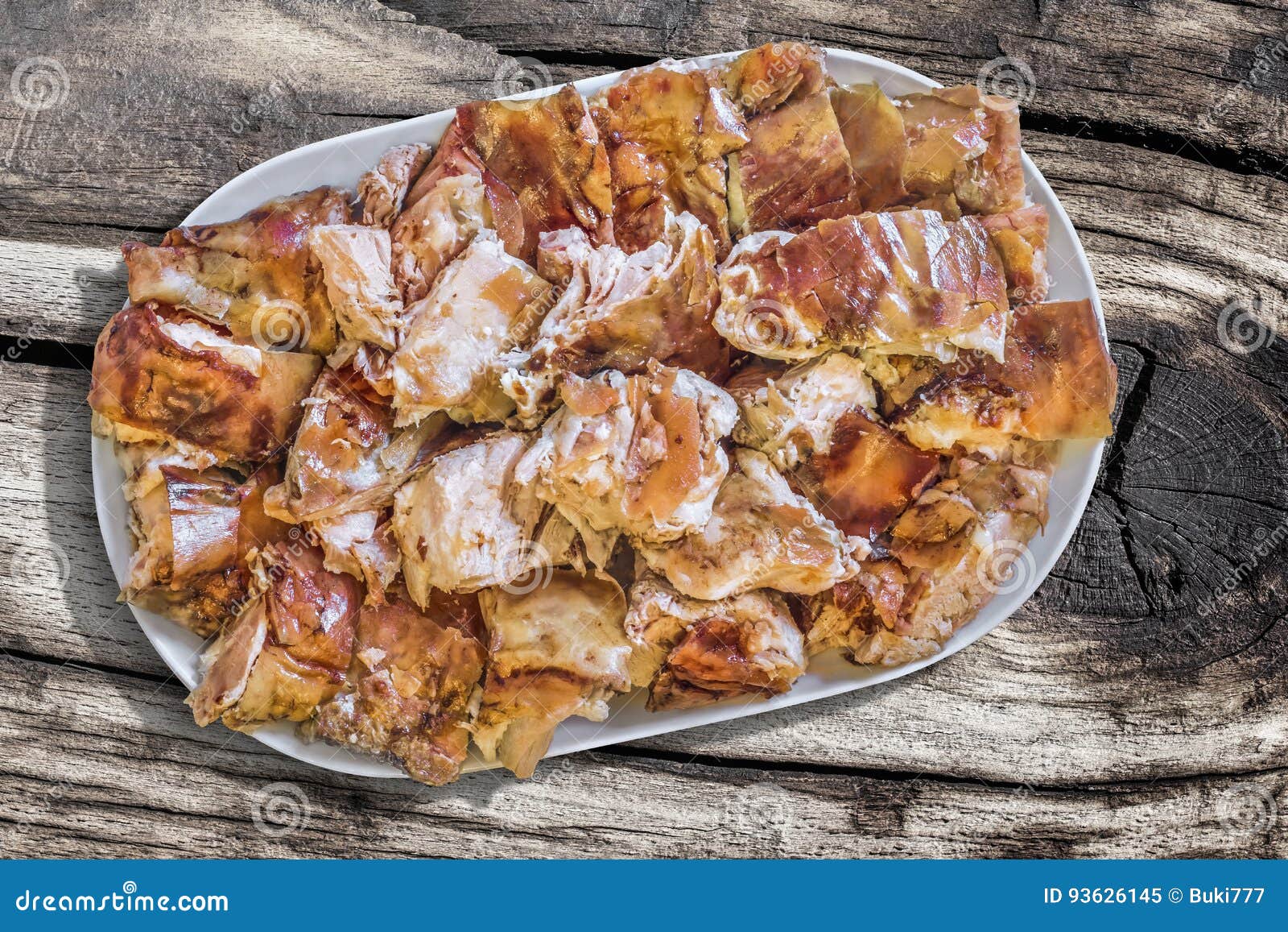plateful of spit roasted pork meat slices set on old knotted cracked wooden picnic table
