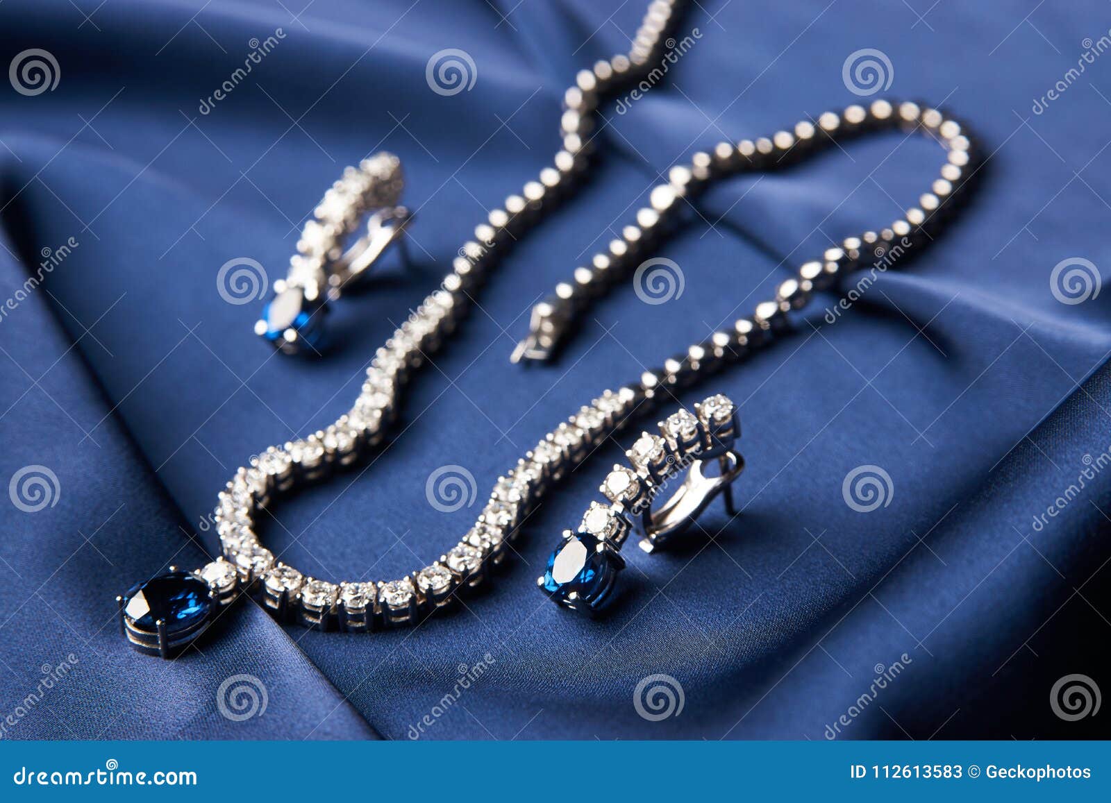 Womens Platinum Necklace And Earrings With A Diamond And Blue Precious  Sapphire Stone On A Silk Blue Background, Close-up. Luxury Female Jewelry  Stock Photo, Picture and Royalty Free Image. Image 97784082.