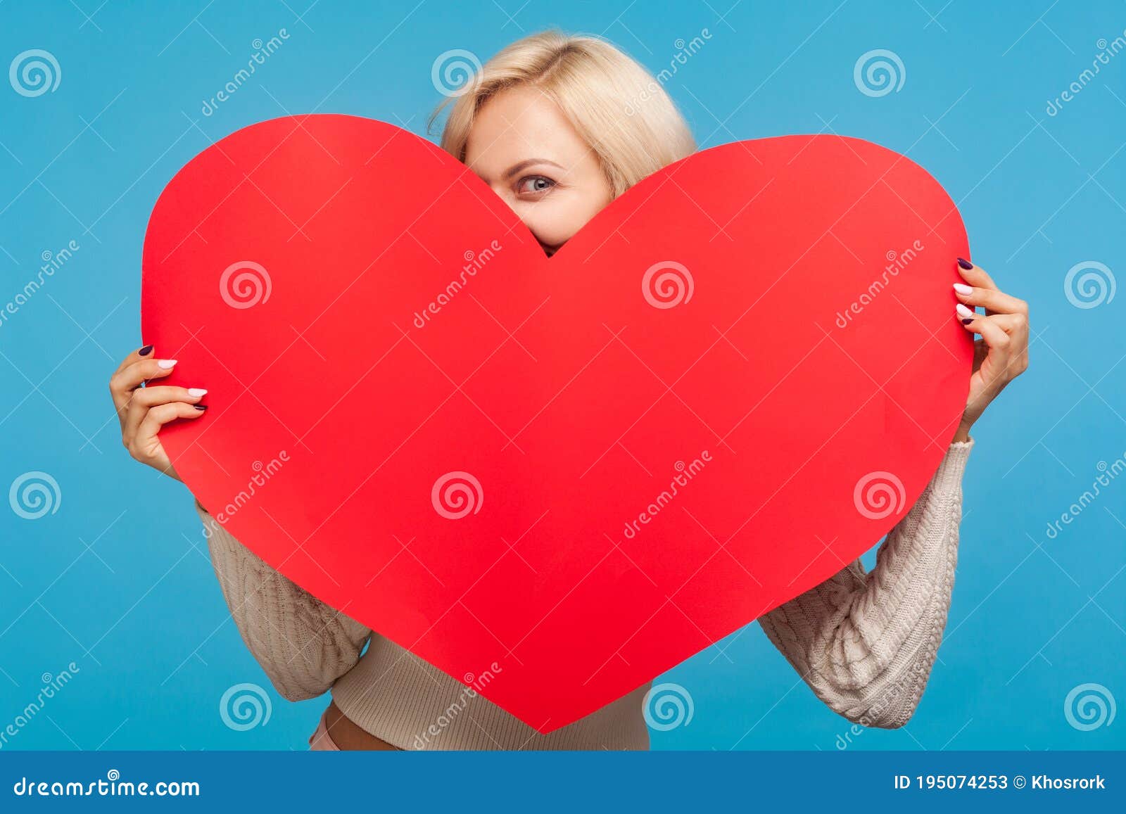 playful blond girl peeping from big paper red heart in her hands, saint valentines day celebration, love and fondness