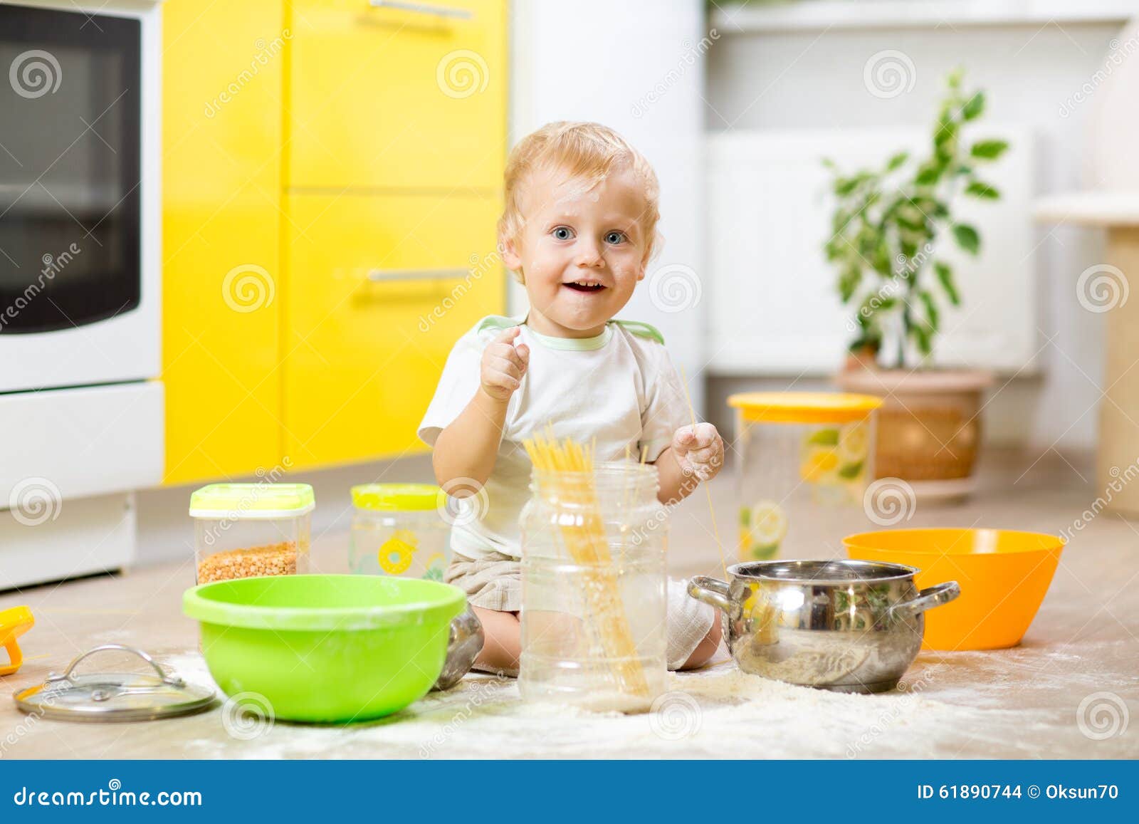 playful kid boy with face in flour surrounded kitchenware and foodstuffs