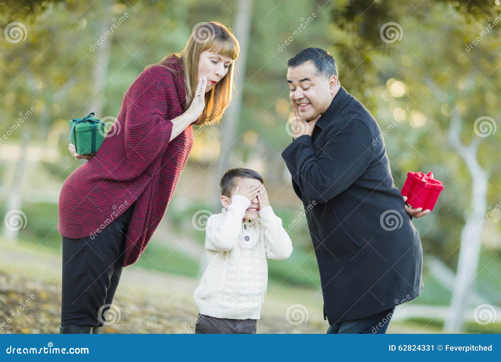 playful mixedrace parents with gifts for young boy hiding eyes