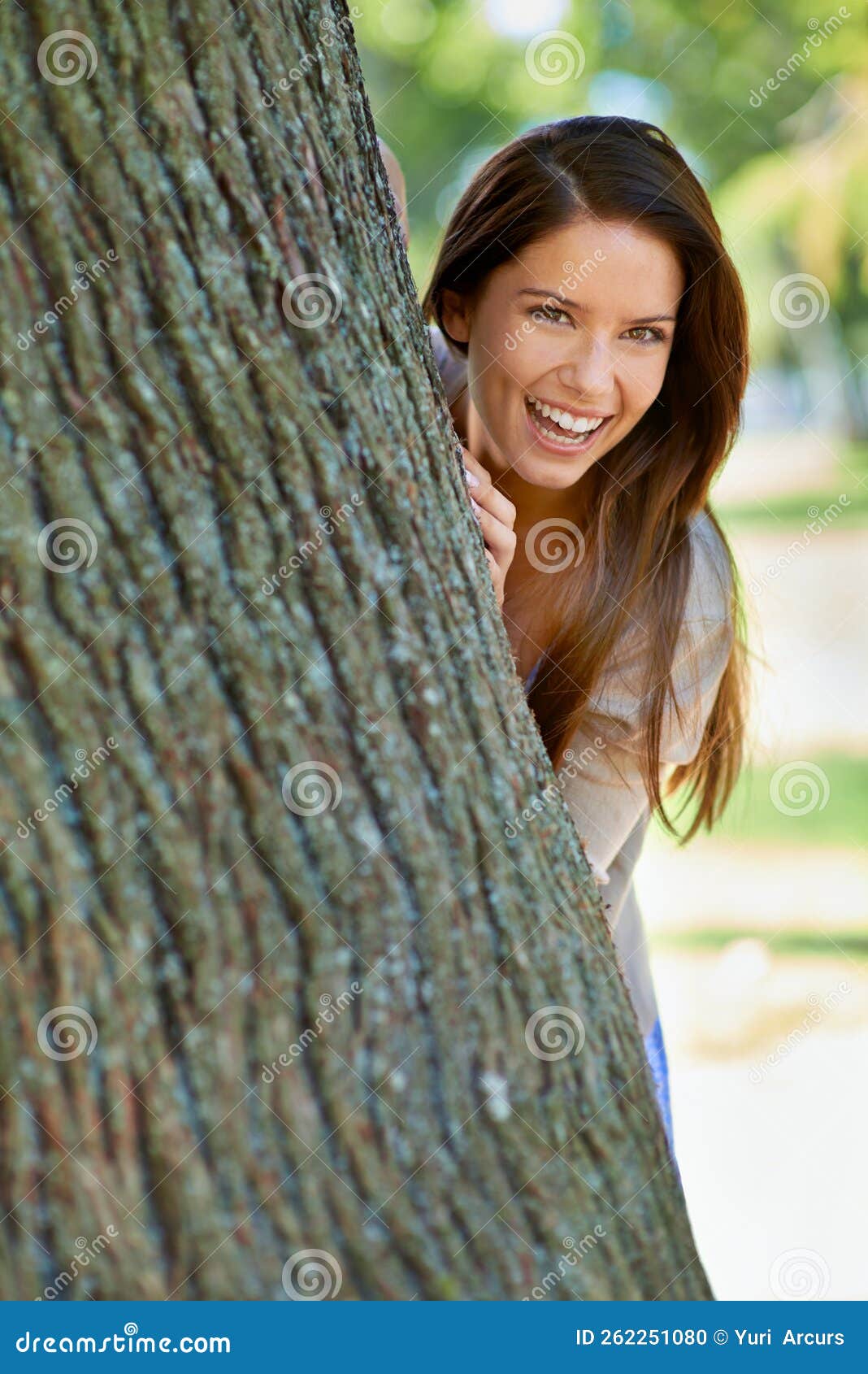 Playful Park Posing Portrait Of A Beautiful Young Woman Standing Behind A Tree At The Park 