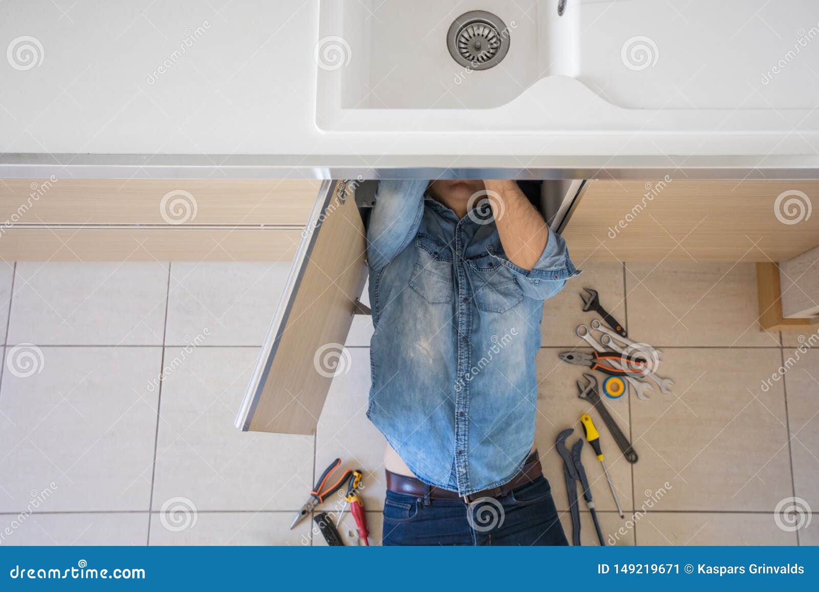 Plumber Working with Broken and Leaking Kitchen Plumbing Stock Image