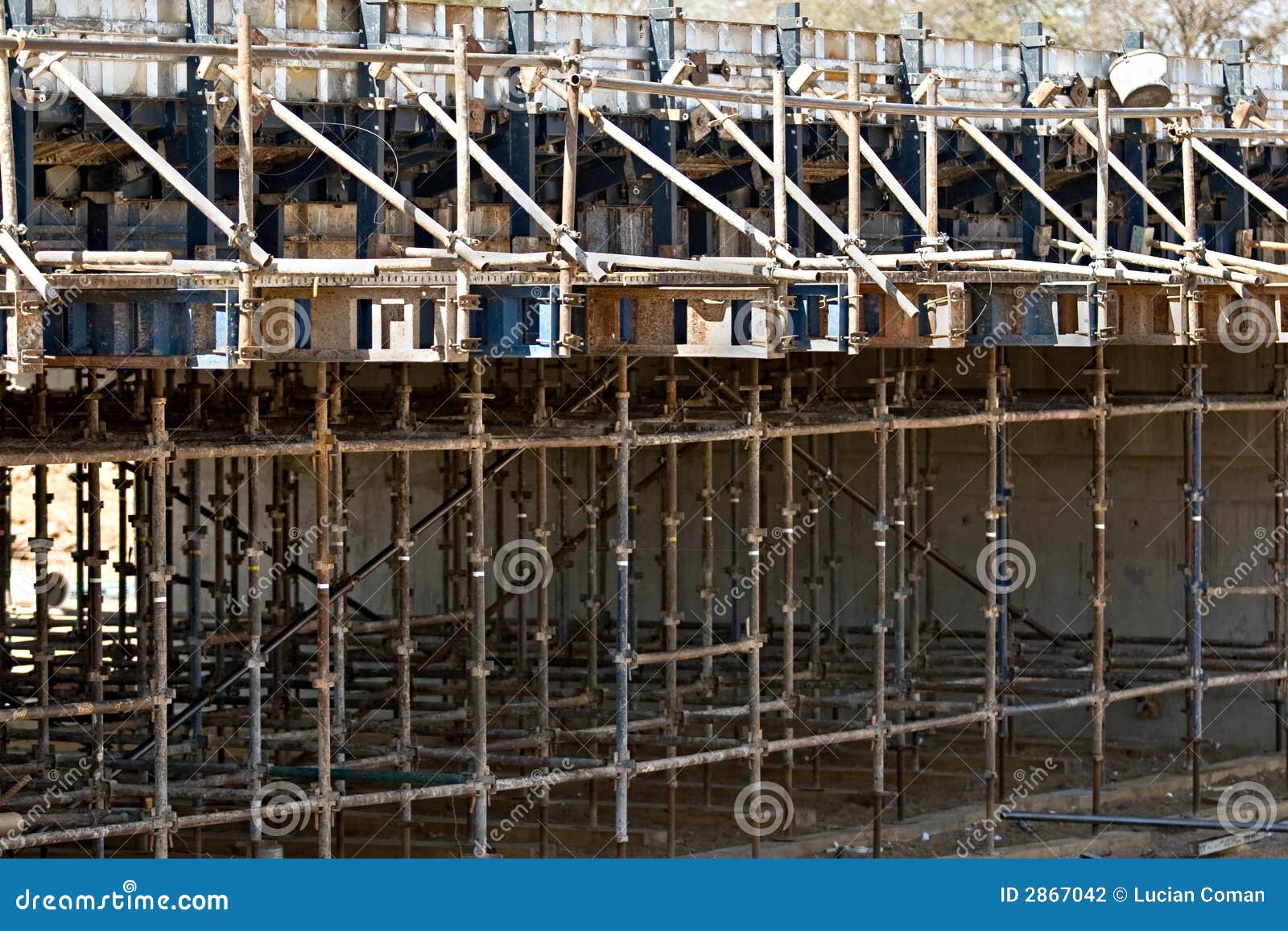 Pólos do andaime em torno da ponte sob a construção sobre o rio com as casas no fundo.