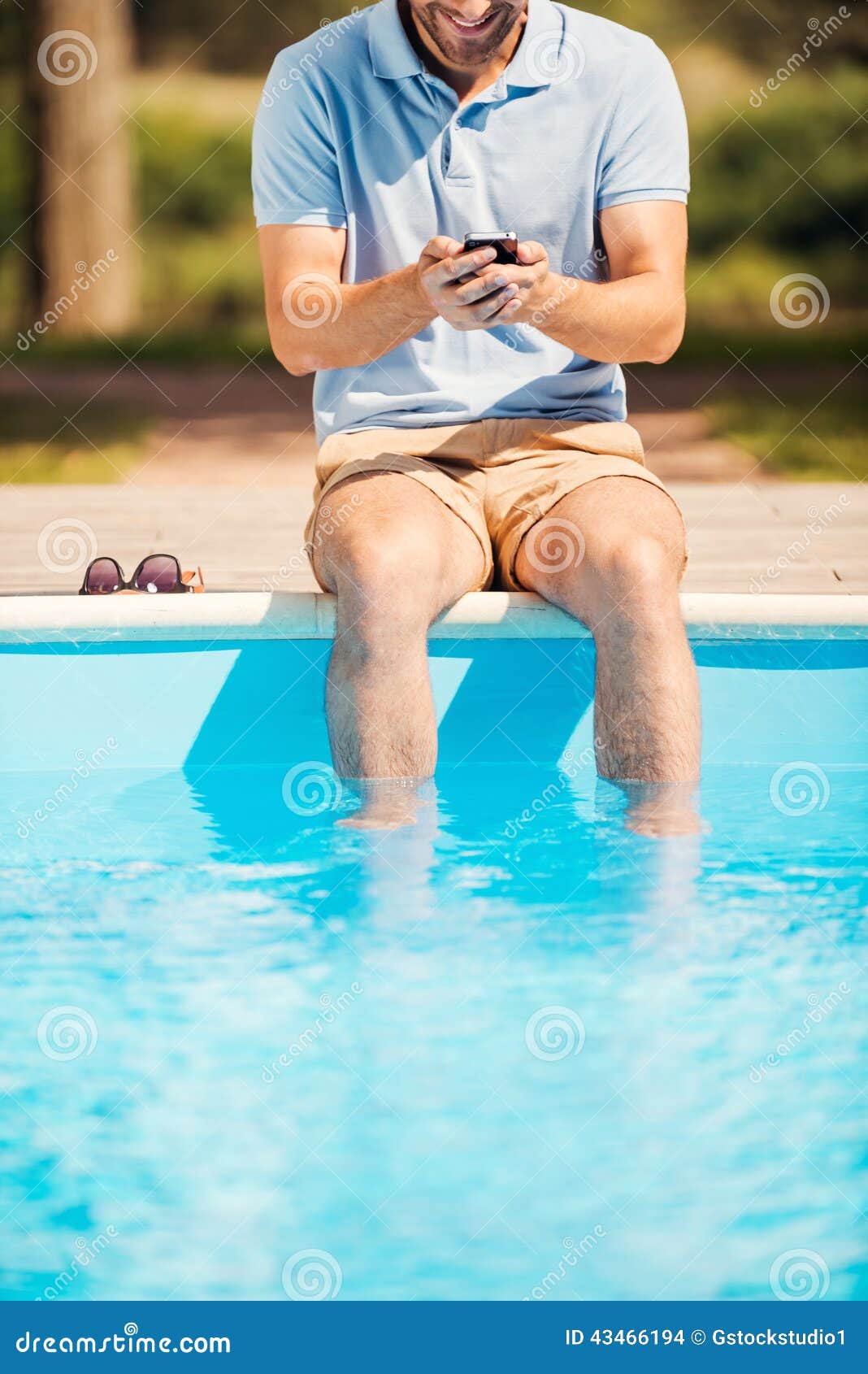 Poolside di rilassamento dell'uomo. Immagine potata del poolside di seduta e di battitura a macchina dell'uomo del qualcosa a macchina sul telefono cellulare