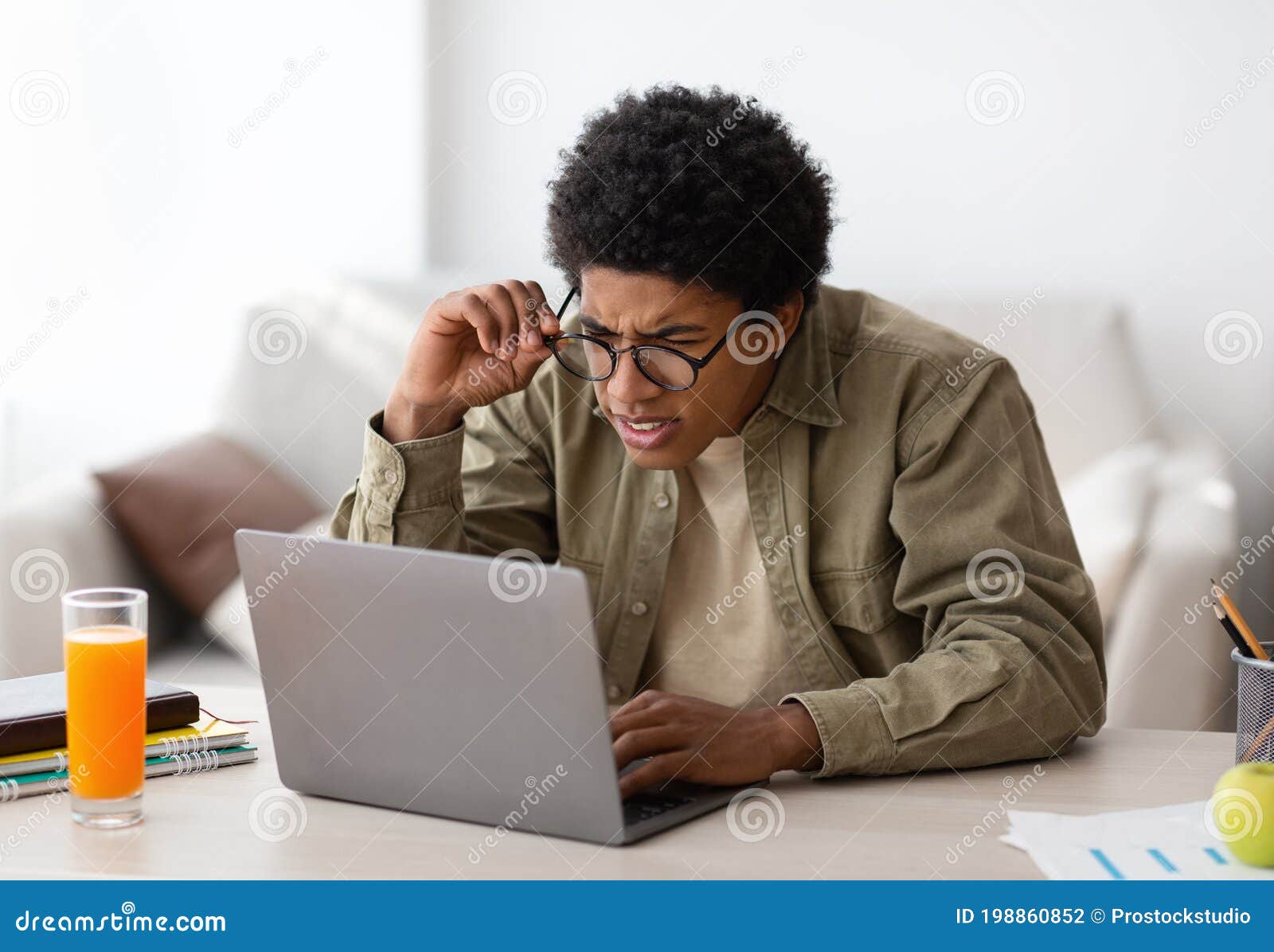 poor eyesight. black teenager in glasses squinting his eyes while using laptop computer for online education at home