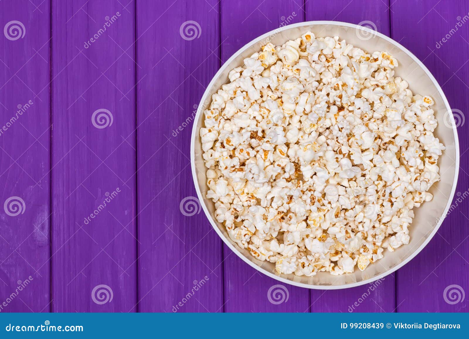 Popcorn in a bowl on purple wooden surface