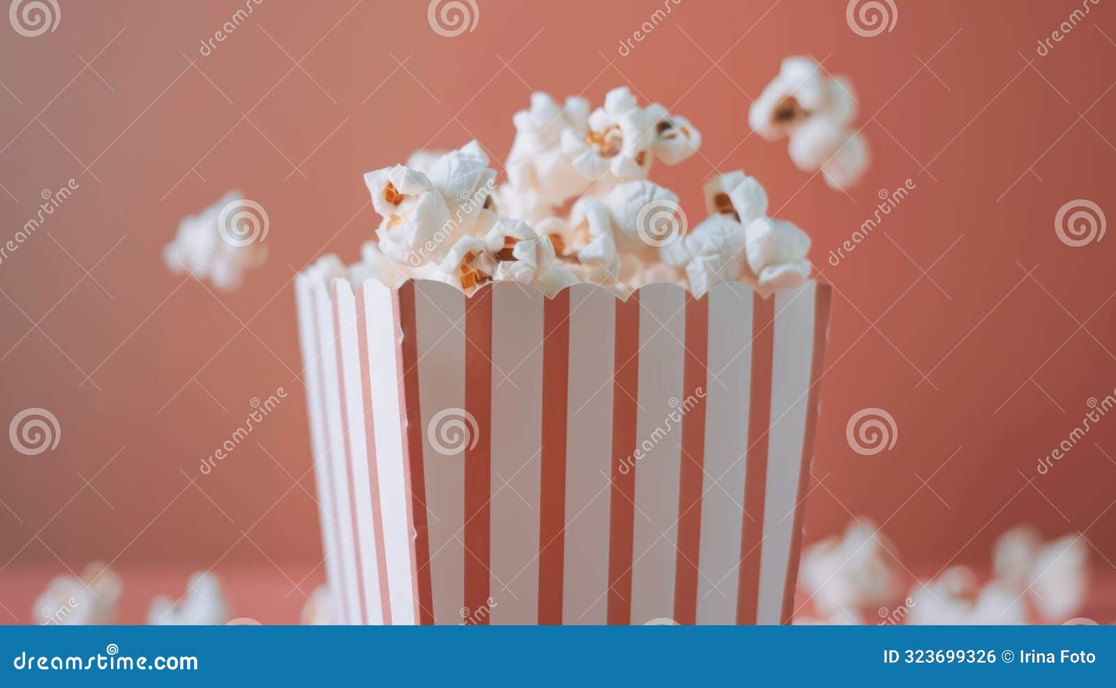 popcorn in a red and white box with pink bokeh background, popcorn kernels in motion.