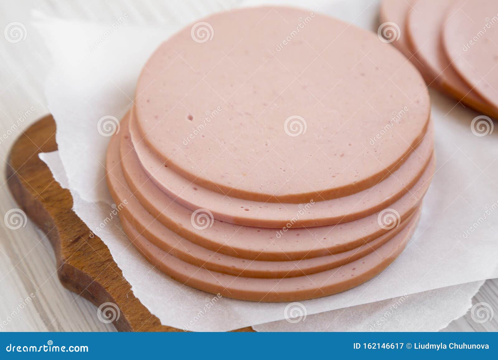 pork bolgna meat slices on a rustic wooden board on a white wooden table, side view. closeup