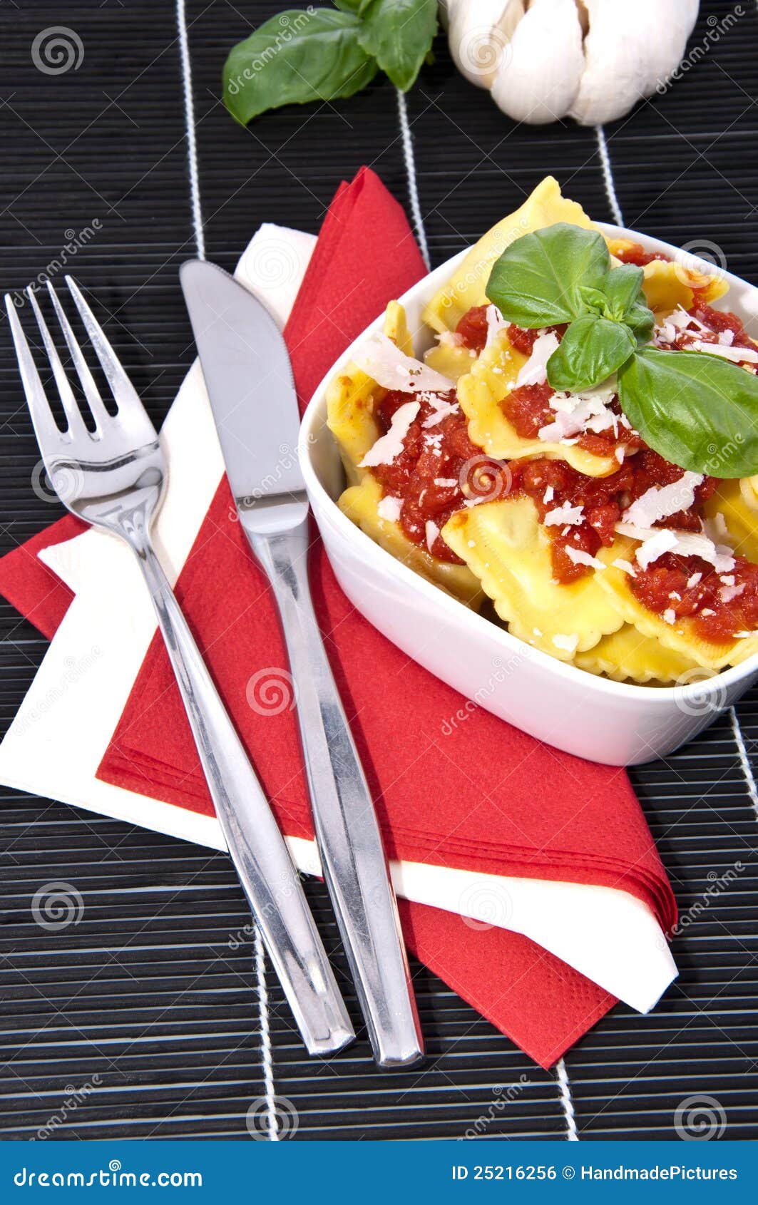 Portion of Raviolis in a bowl. Portion of Raviolis with tomato sauce and Parmesan Cheese in a bowl with raw ingredients in the background on a black tablecloth