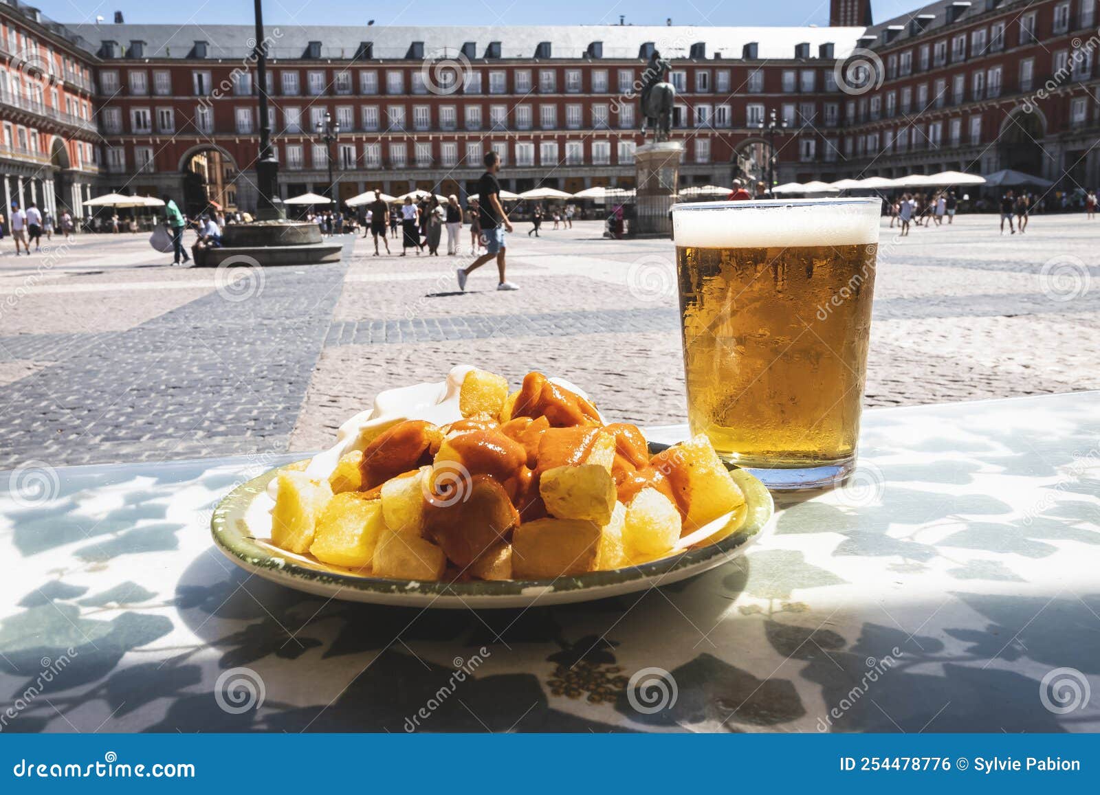 a portion of tapas in the plaza mayor in madrid. potatoes with alioli sauce and brava sauce with a beer.