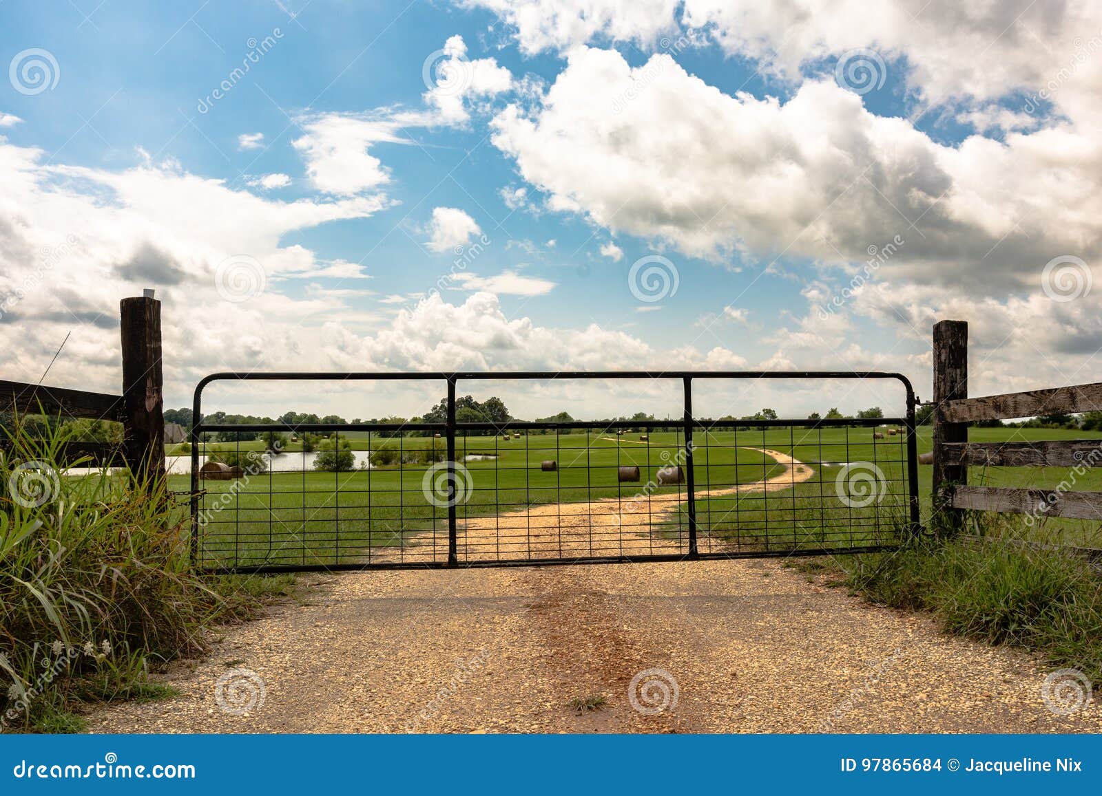 Portone del metallo sulla strada non asfaltata. Metal il portone chiuso su una strada non asfaltata che conduce in un campo Lo stagno dell'azienda agricola e le balle di fieno rotonde sono visibili nei precedenti