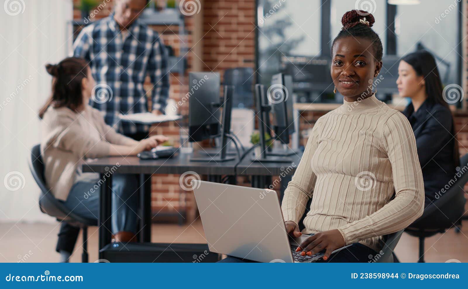 portrait of african american coder sitting down writing programming language on laptop looking up and smiling