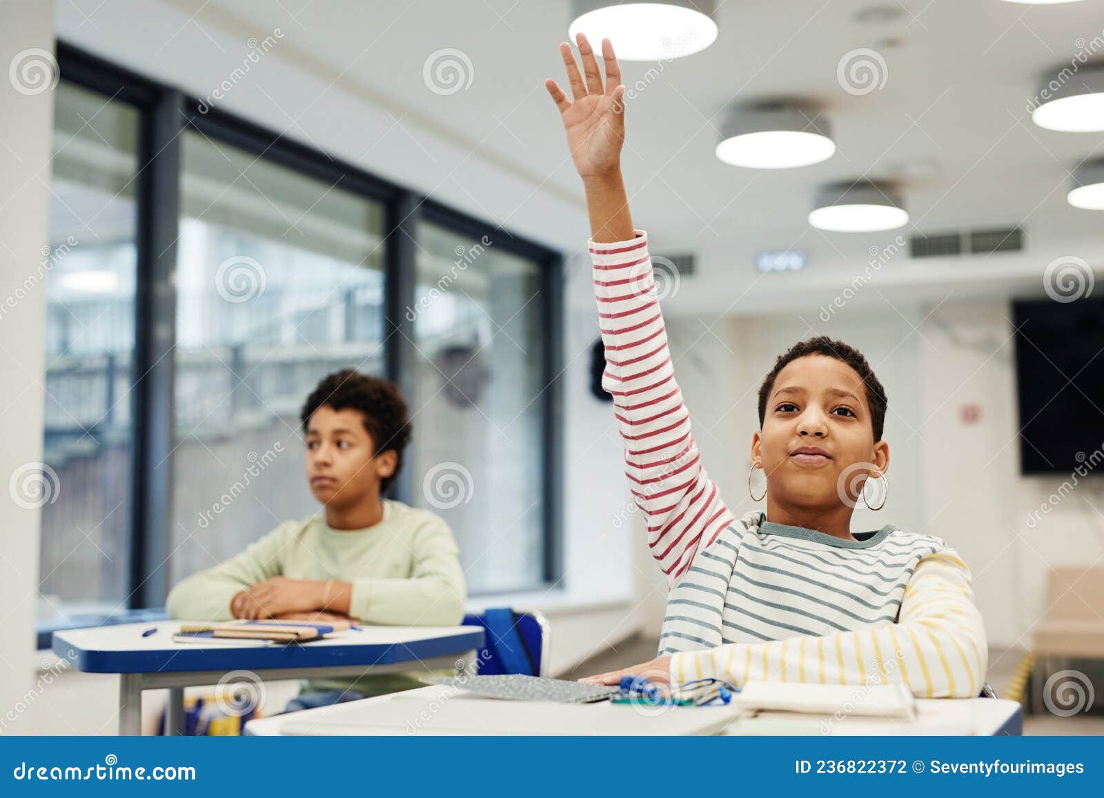 Girl Raising Hand in Class. Portrait of African-American girl with short hair raising hand in modern classroom, copy space