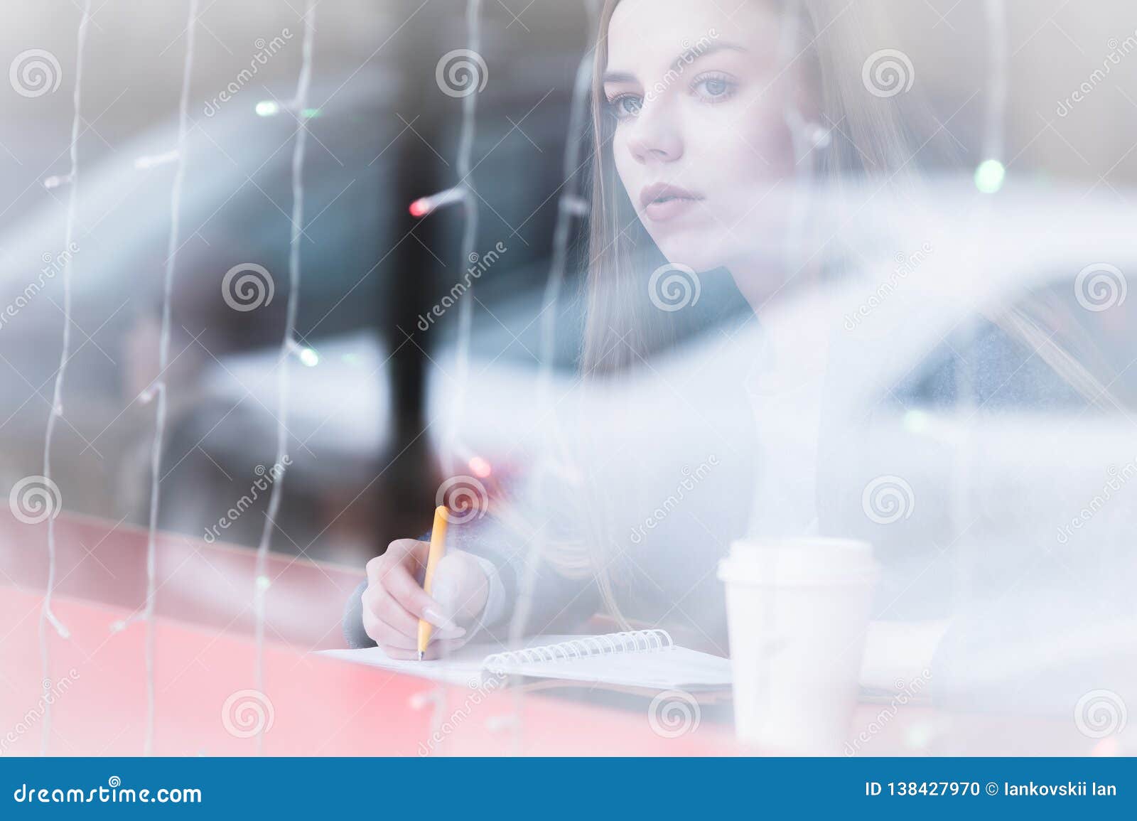 portrait of an attractive young journalist girl with pen and notepad in cafe behind the showcase. non-contrast view
