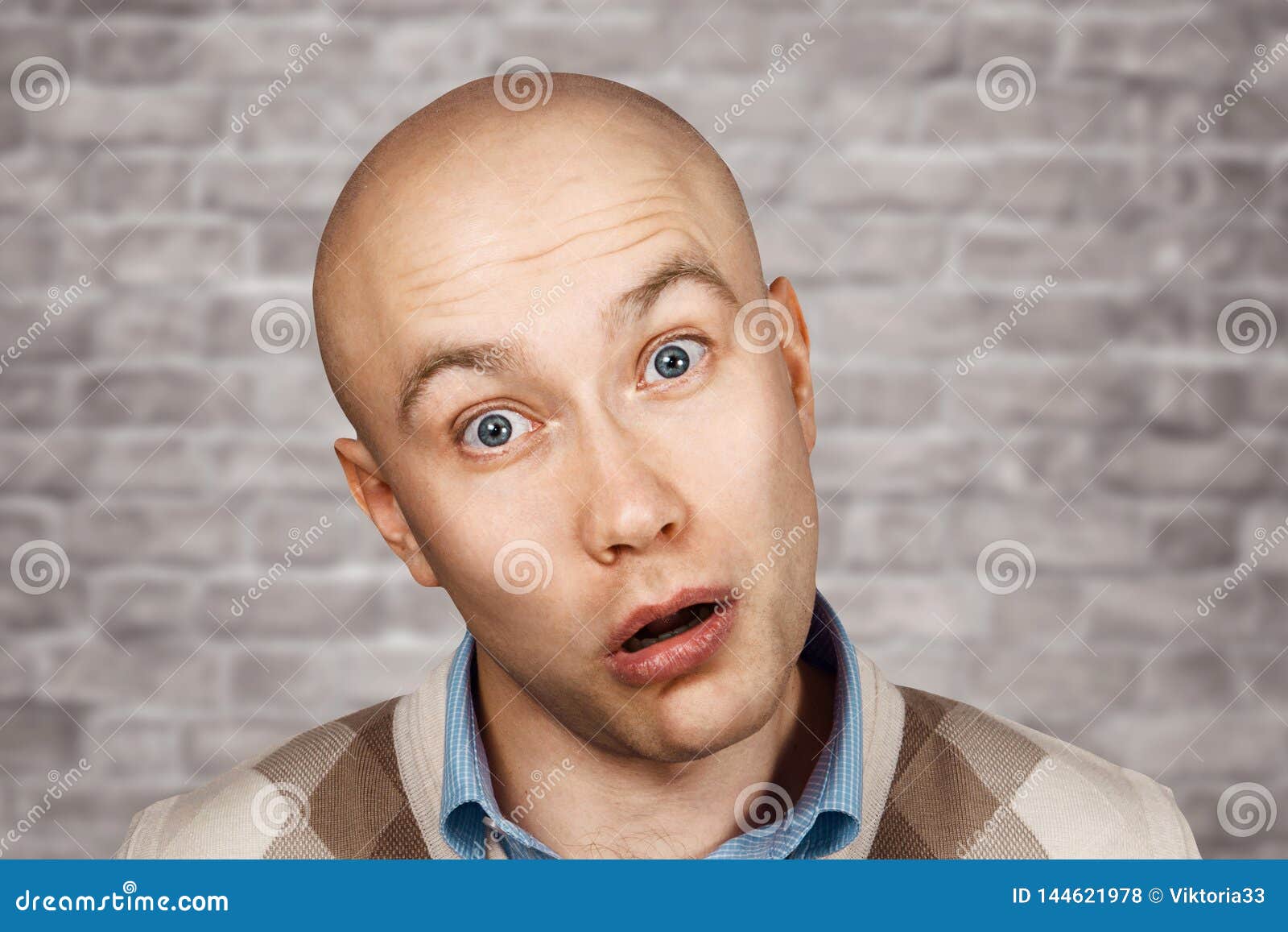 portrait of a bald stupid surprised guy with open mouth on an brick wall background
