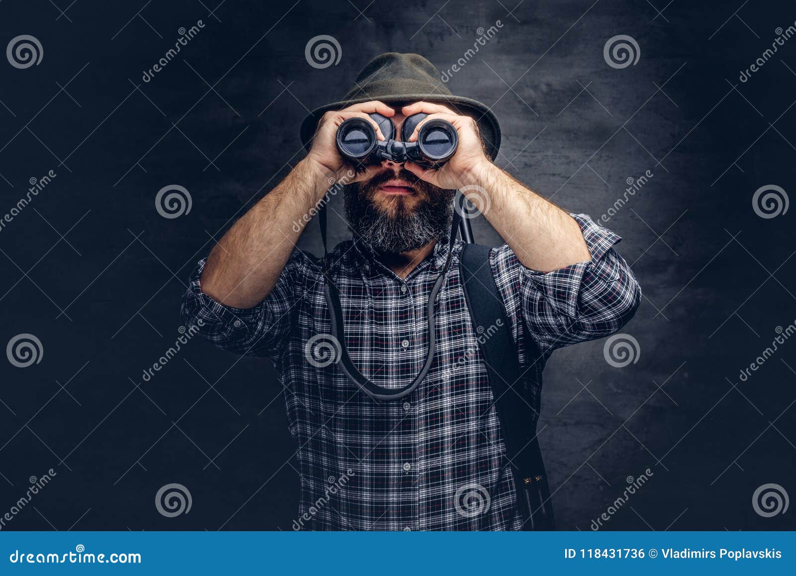 portrait of a bearded hunter traveler tries to find prey while looking through binoculars.