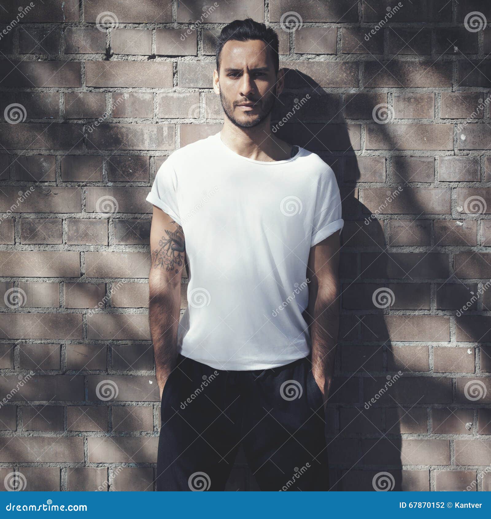 portrait bearded man with tattoo wearing blank white tshirt and black jeans. bricks wall background. vertical mockup
