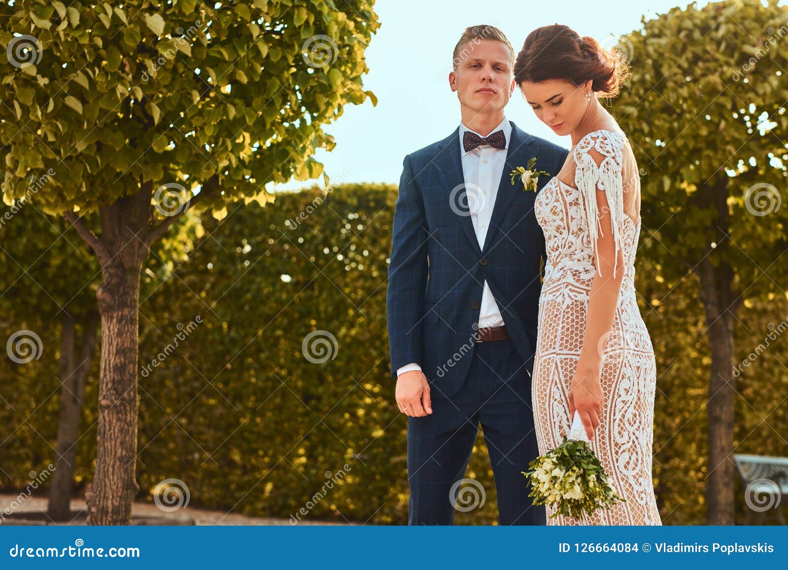Portrait of beautiful newlyweds - charming bride embrace her handsome groom in the park.