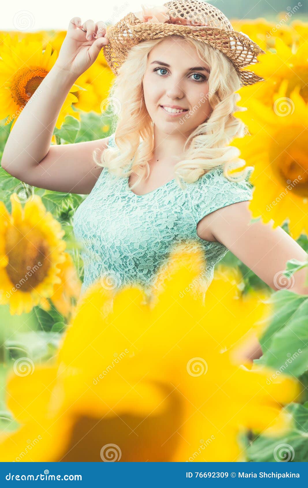 Portrait of a beautiful smiling blonde girl in a straw hat outdoors in a field of sunflowers