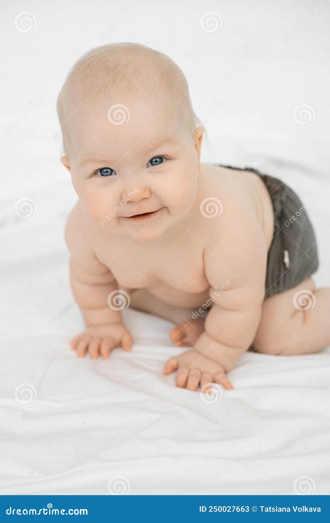 portrait of beautiful smiling grey-eyed plump cherubic baby infant toddler wearing grey pants standing on all fours.
