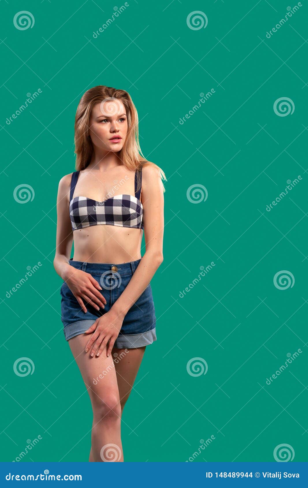 Portrait of a beautiful young Caucasian woman 20 years old model in a black and white swimsuit and denim shorts with natural make-up posing on green isolated background