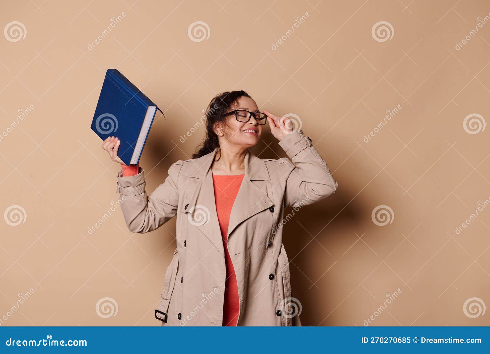 portrait on beige background of a smiling multi-ethnic middle-aged female educator, school teacher with a harcover book