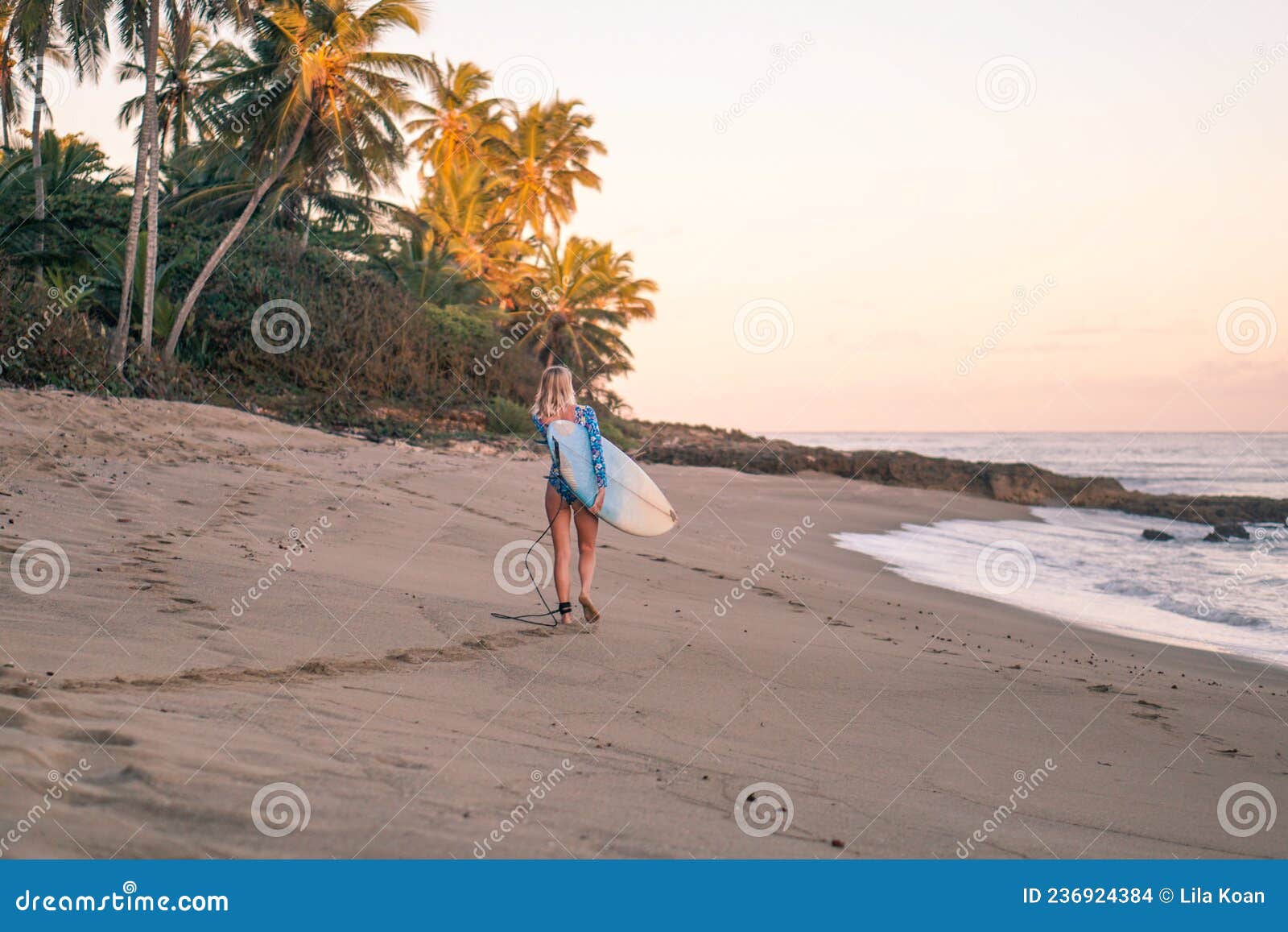 portrait of blond surfer girl with white surf board in blue ocean pictured from the water in encuentro beach