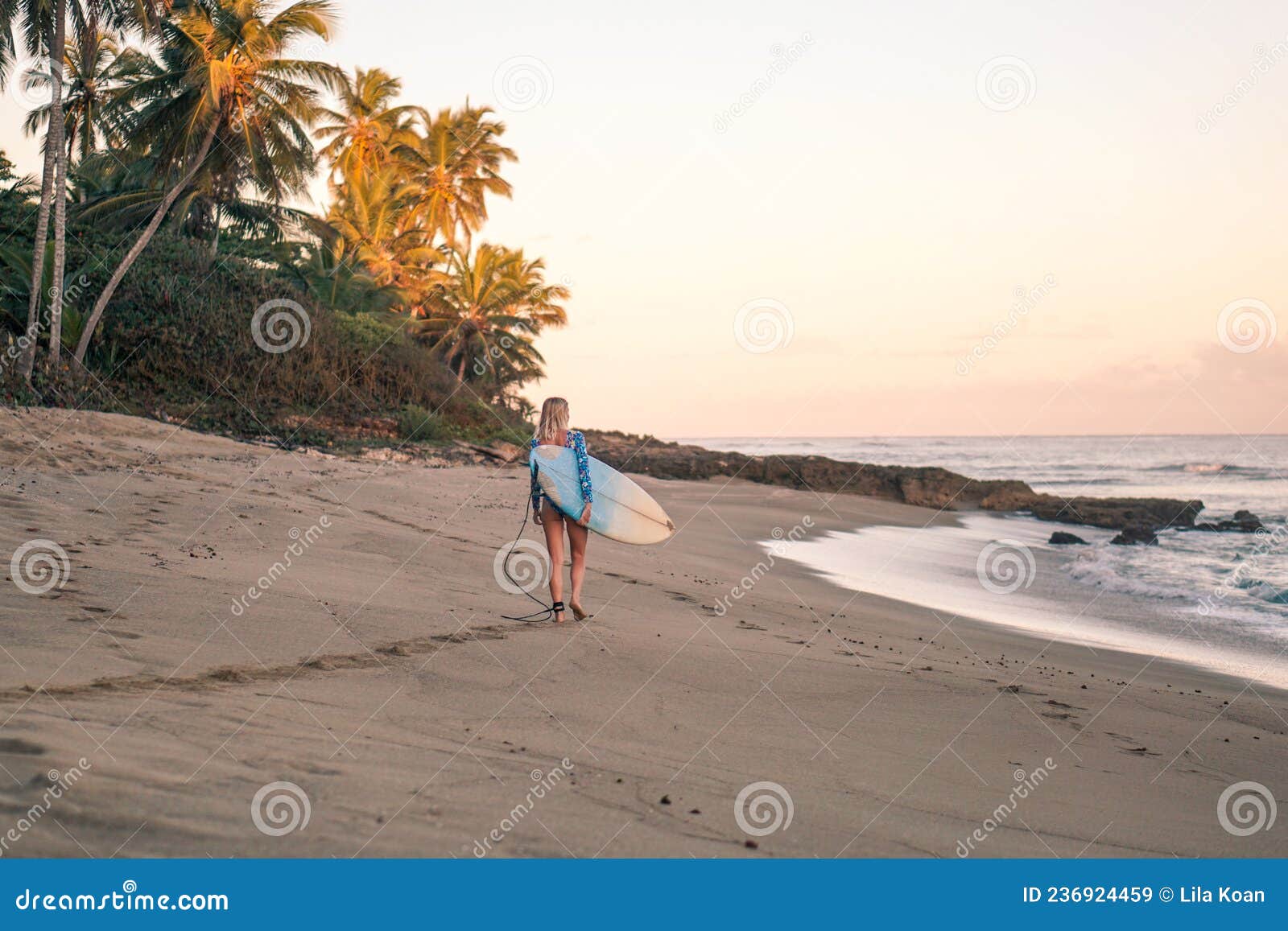 portrait of blond surfer girl with white surf board in blue ocean pictured from the water in encuentro beach