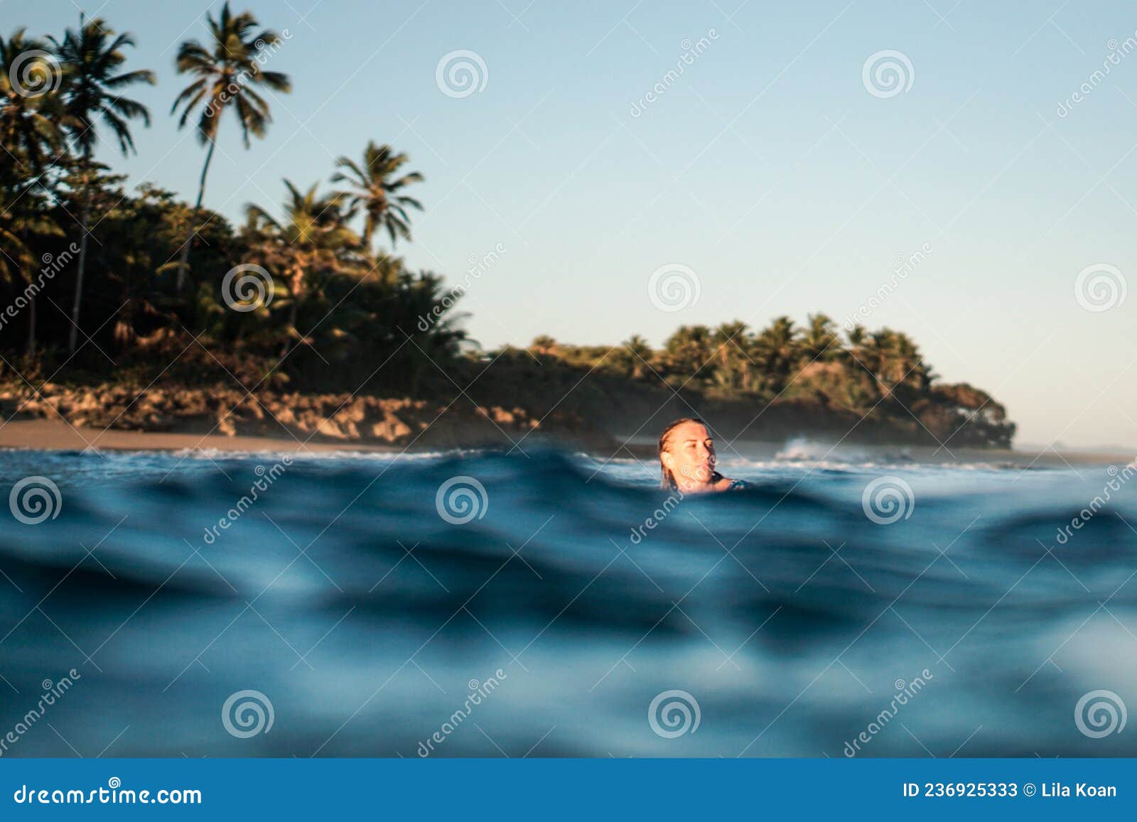 portrait of blond surfer girl on white surf board in blue ocean pictured from the water in encuentro beach