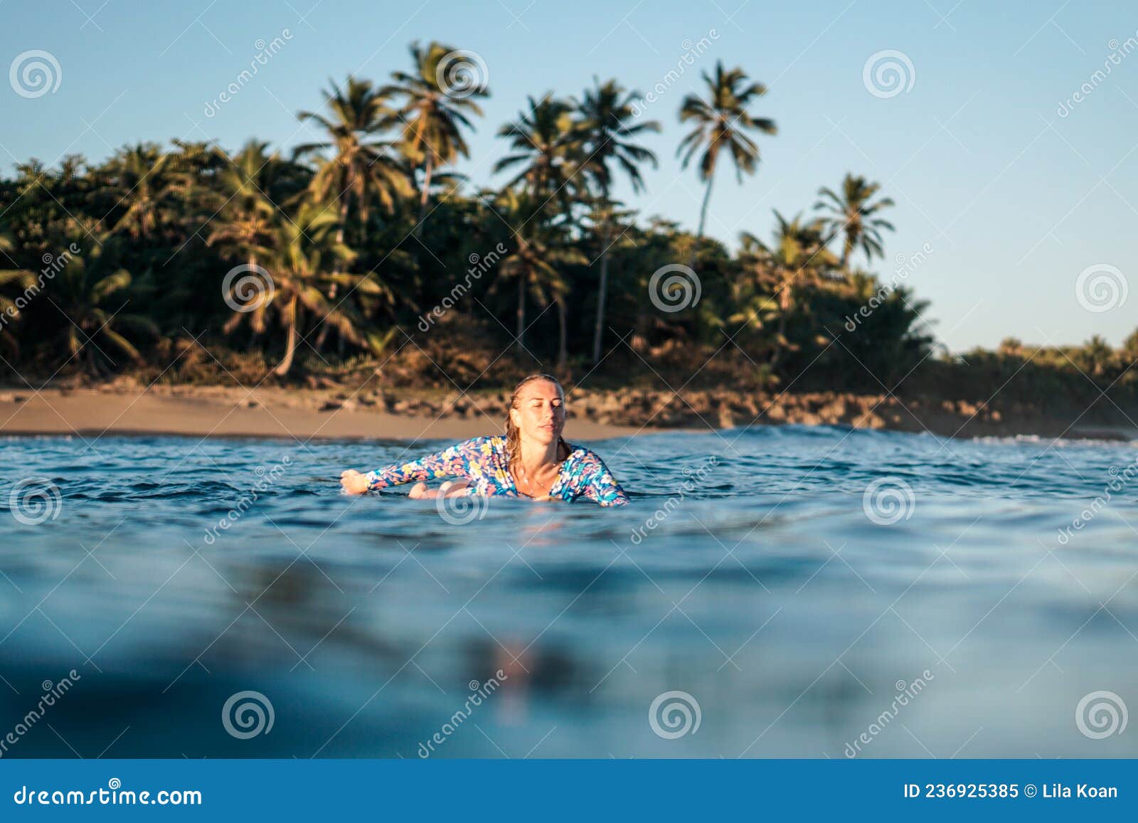 portrait of blond surfer girl on white surf board in blue ocean pictured from the water in encuentro beach