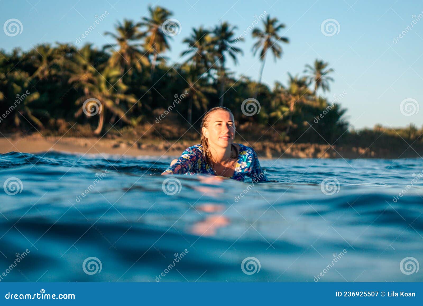 portrait of blond surfer girl on white surf board in blue ocean pictured from the water in encuentro beach