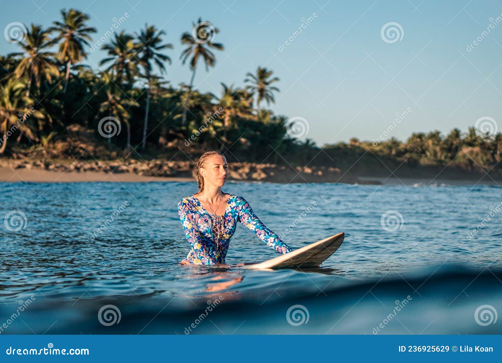 portrait of blond surfer girl on white surf board in blue ocean pictured from the water in encuentro beach