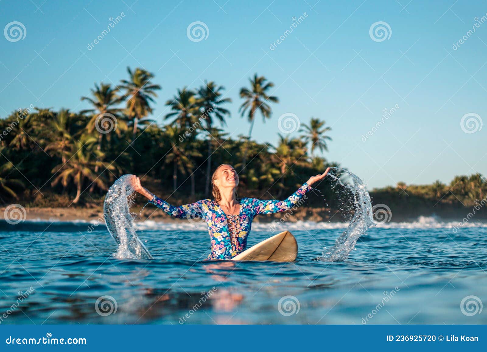 portrait of blond surfer girl on white surf board in blue ocean pictured from the water in encuentro beach