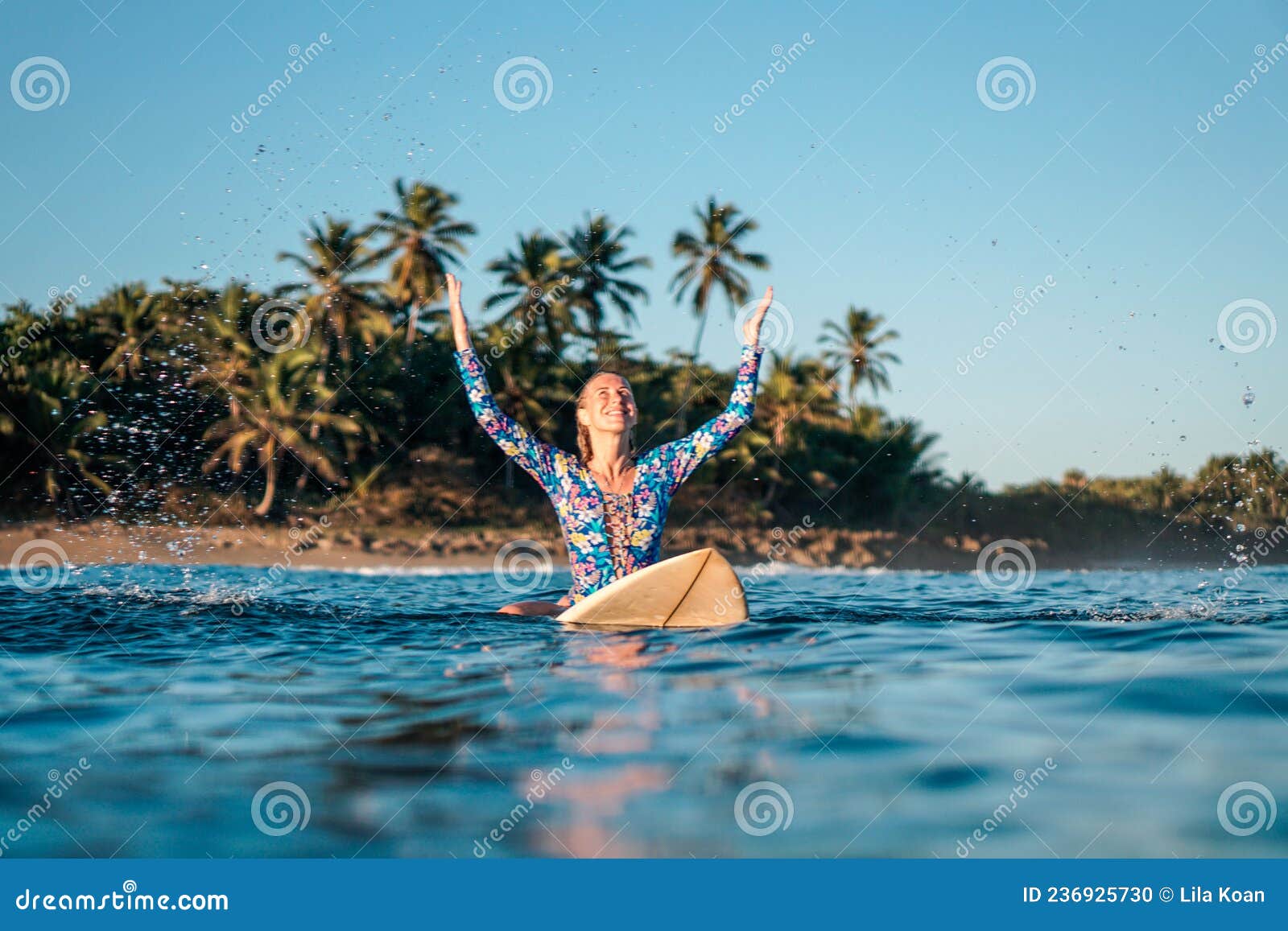 portrait of blond surfer girl on white surf board in blue ocean pictured from the water in encuentro beach