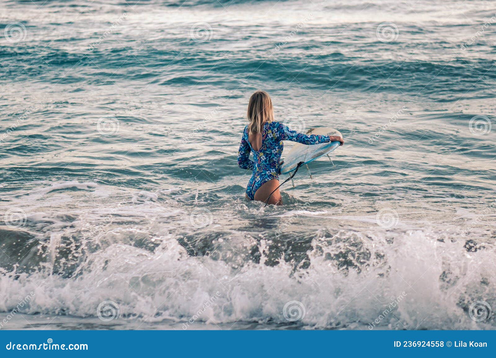 portrait of blond surfer girl with white surf board in blue ocean pictured from the water in encuentro beach