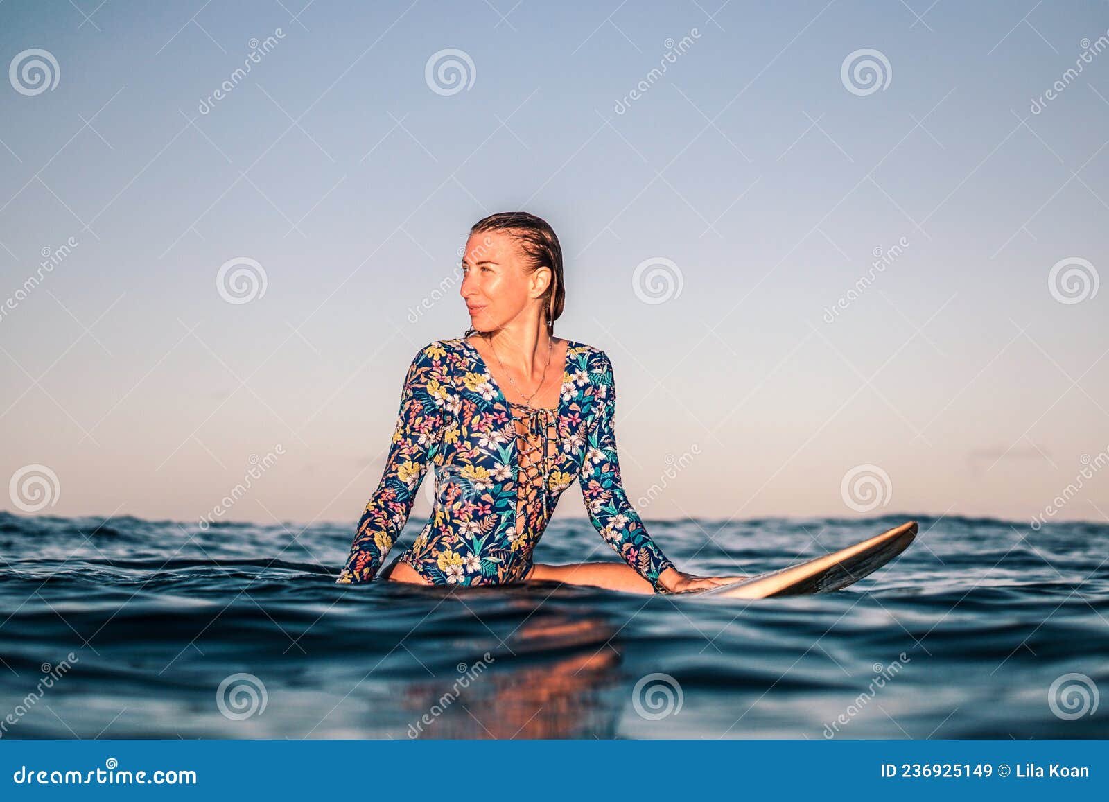 portrait of blond surfer girl on white surf board in blue ocean pictured from the water in encuentro beach