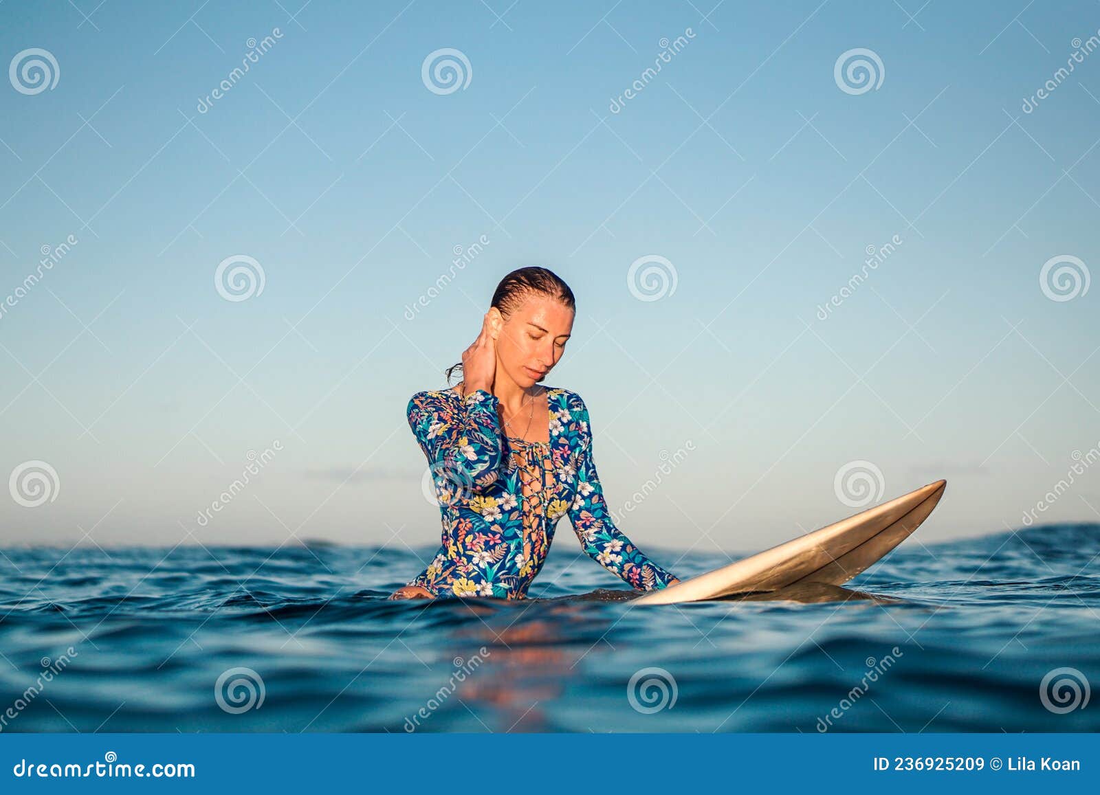 portrait of blond surfer girl on white surf board in blue ocean pictured from the water in encuentro beach