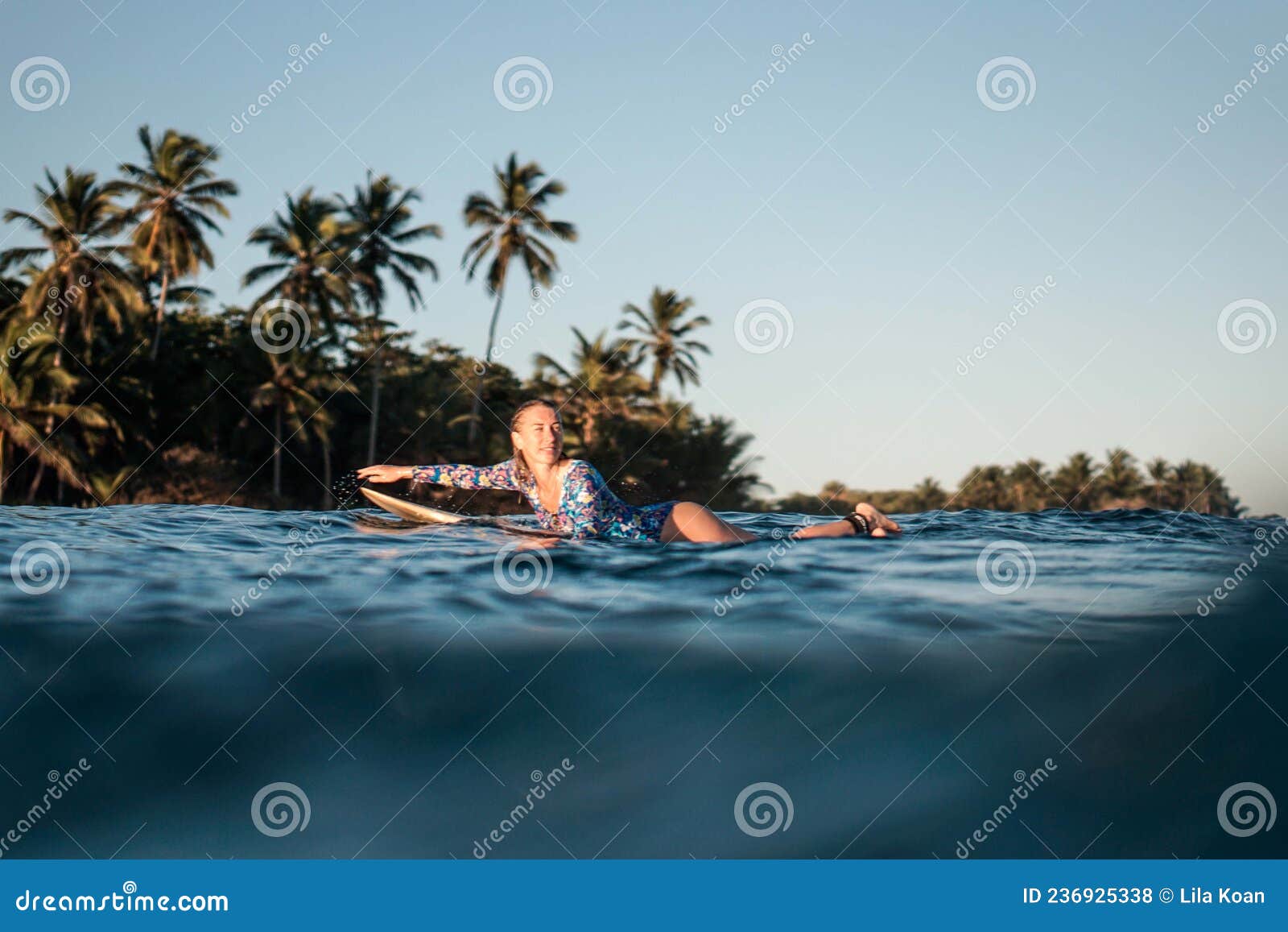 portrait of blond surfer girl on white surf board in blue ocean pictured from the water in encuentro beach