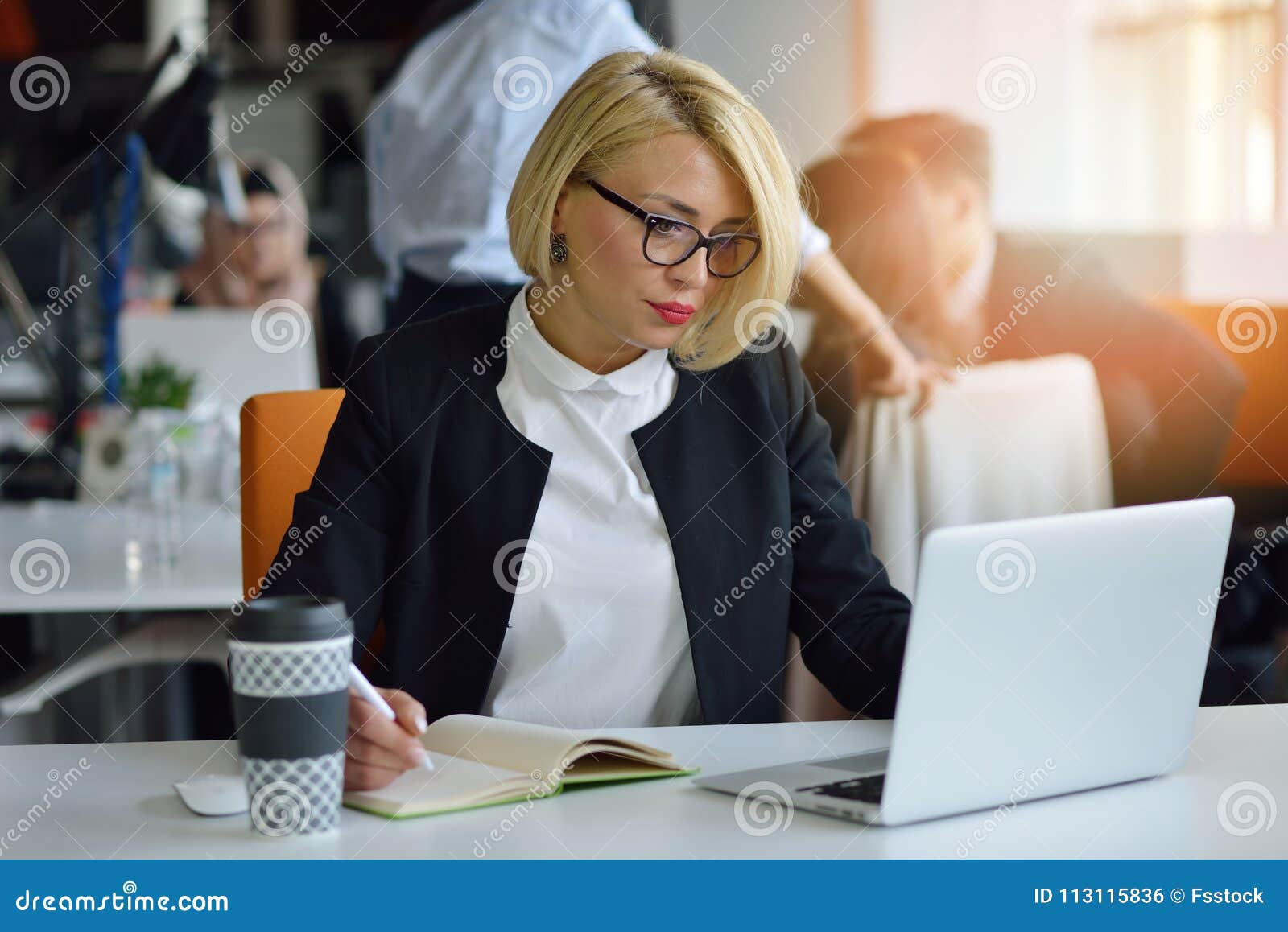 portrait of a blonde female business partner in her 30`s sitting at her tidy desk in front of her computer.