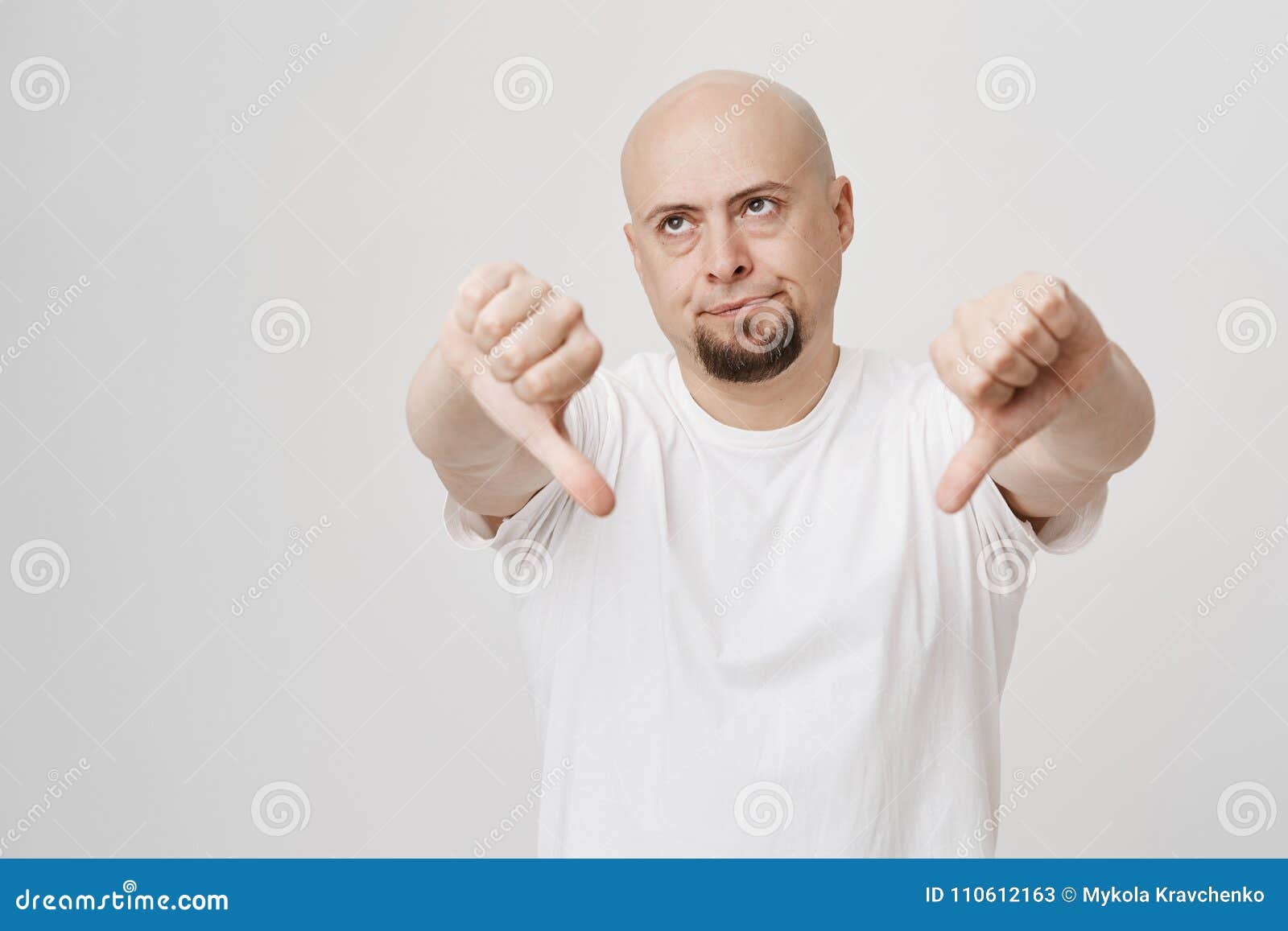 portrait of bothered annoyed bald caucasian bearded man showing thumbs down, giving negative opinion while rolling eyes