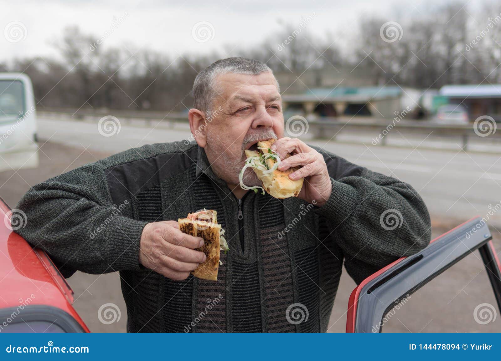 caucasian senior driver gobbling lyulya kebab in lavash near his car