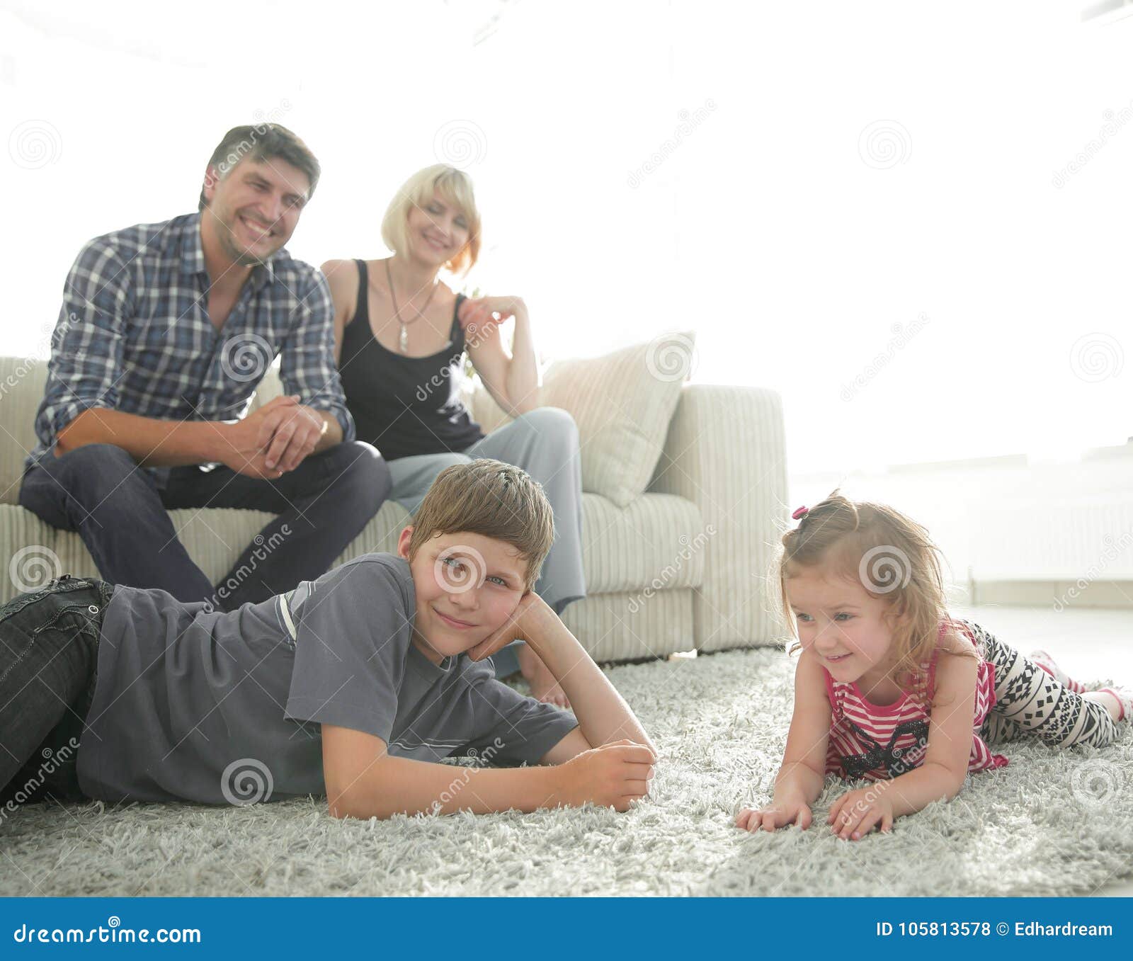Portrait Of Children While Parents Sitting At Sofa In Living Roo Stock