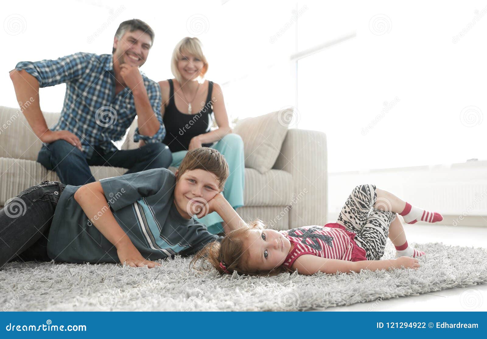 Portrait Of Children While Parents Sitting At Sofa In Living Roo Stock