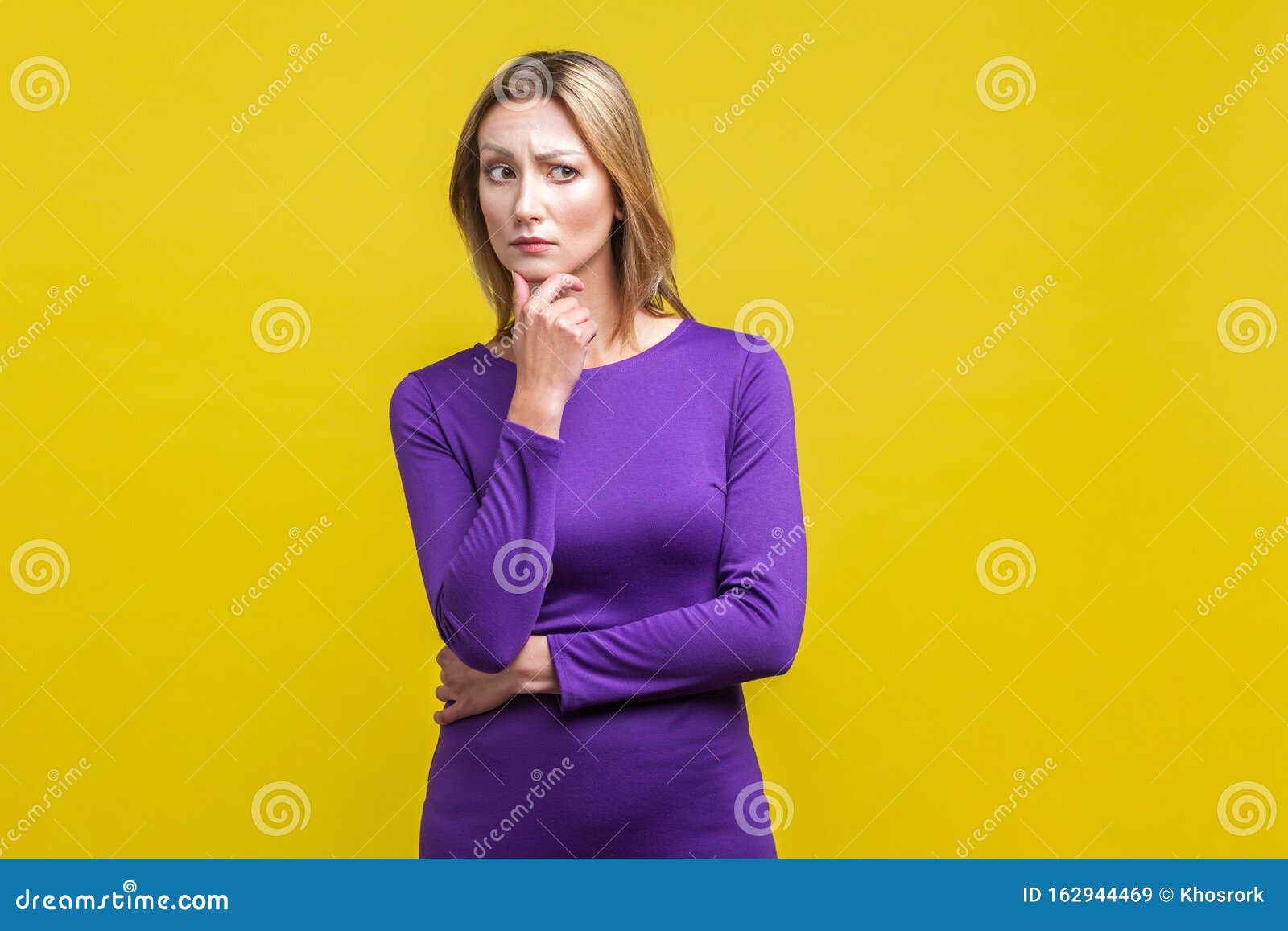 portrait of confused puzzled woman holding her chin while thinking intensely.  on yellow background