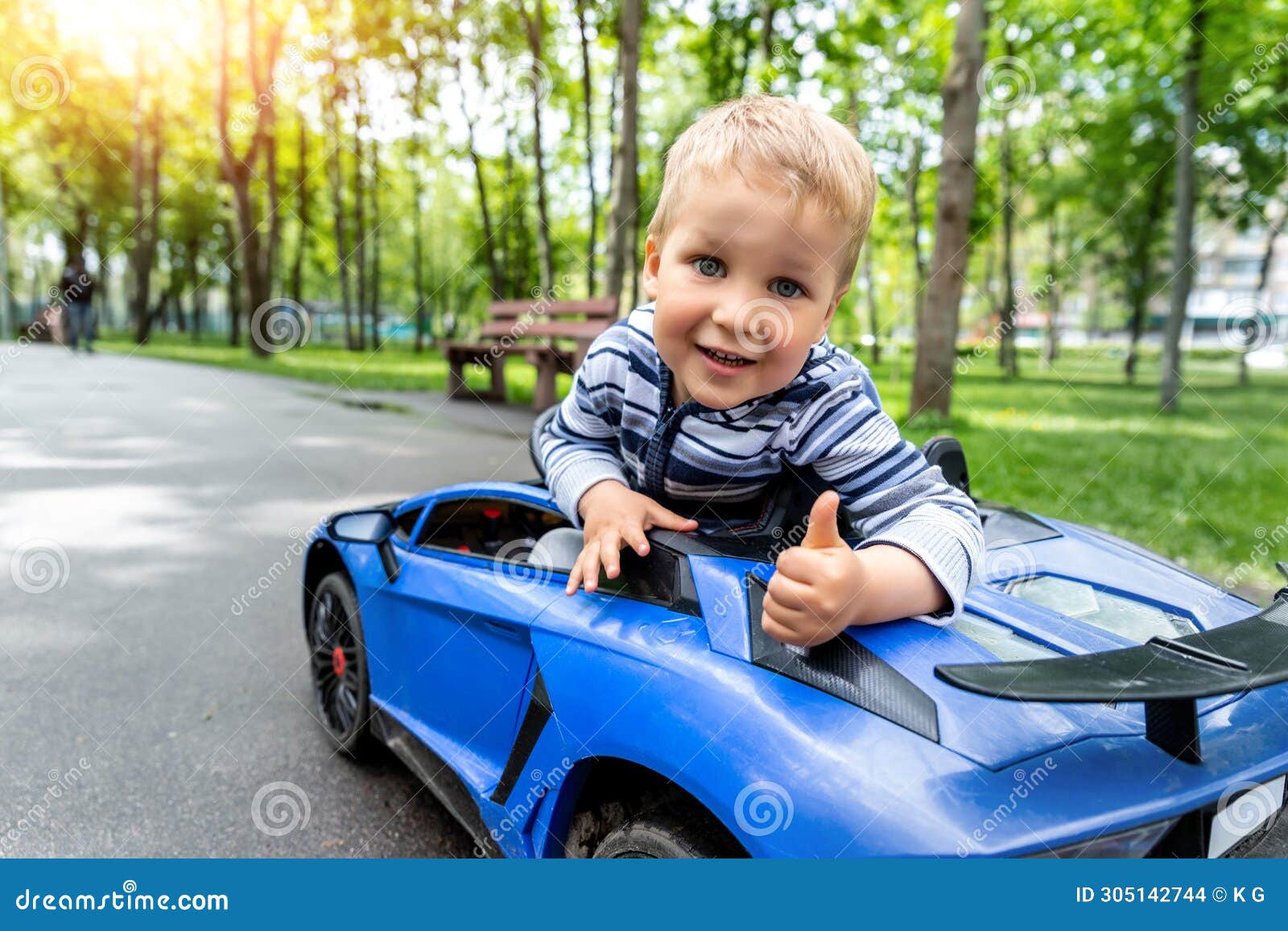portrait of cute little caucasain blond toddler boy enjoy having fun riding electric powered toy car by asphalt path
