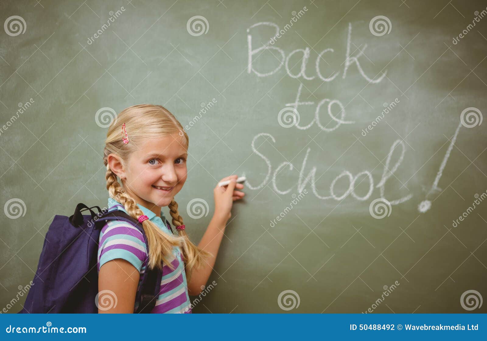 Portrait of cute little girl writing on blackboard in the classroom